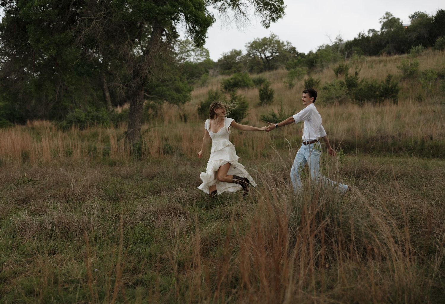 Couple dancing together in a rustic field with tall grass at sunset.