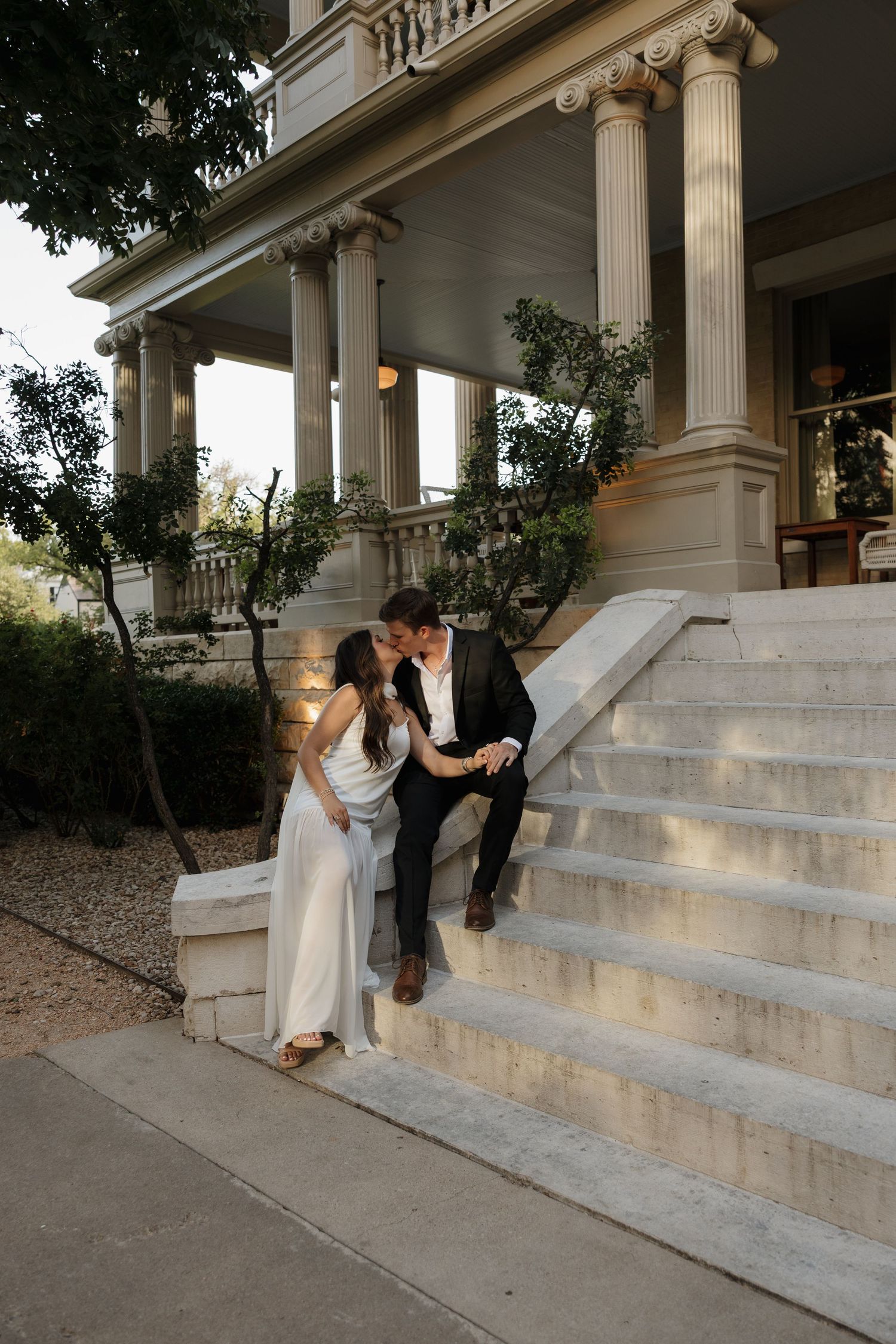 A couple in wedding attire sharing an intimate moment on grand white columned steps of a historic building.