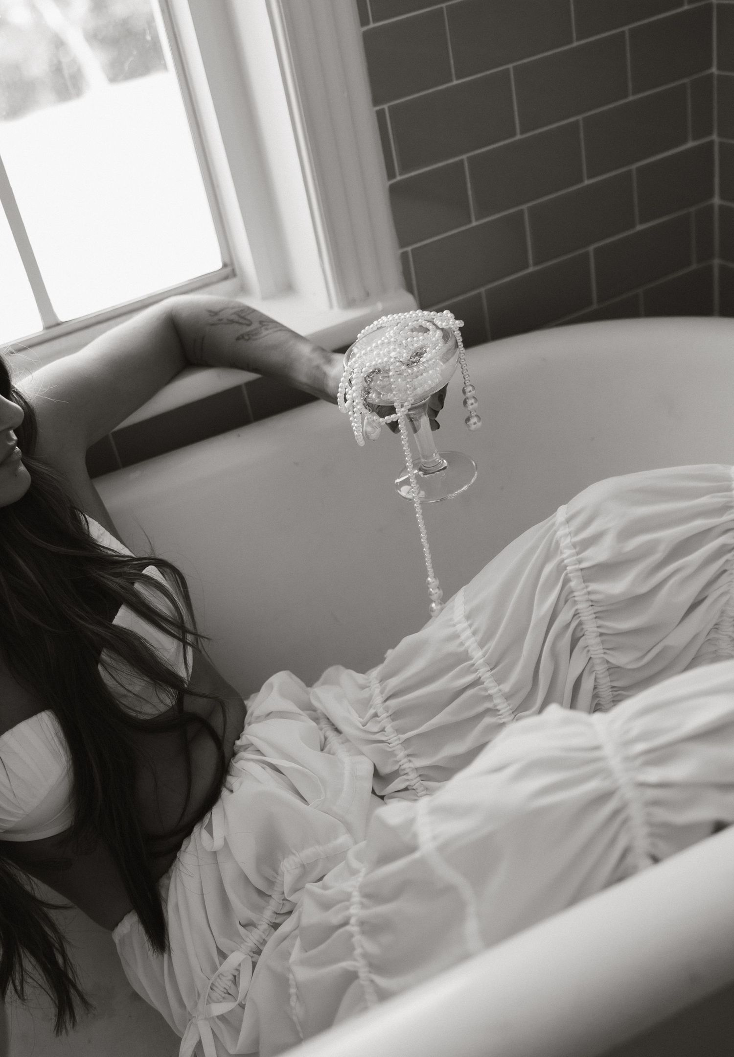 A dreamy black and white photo of a person in a white dress relaxing in a bathtub.