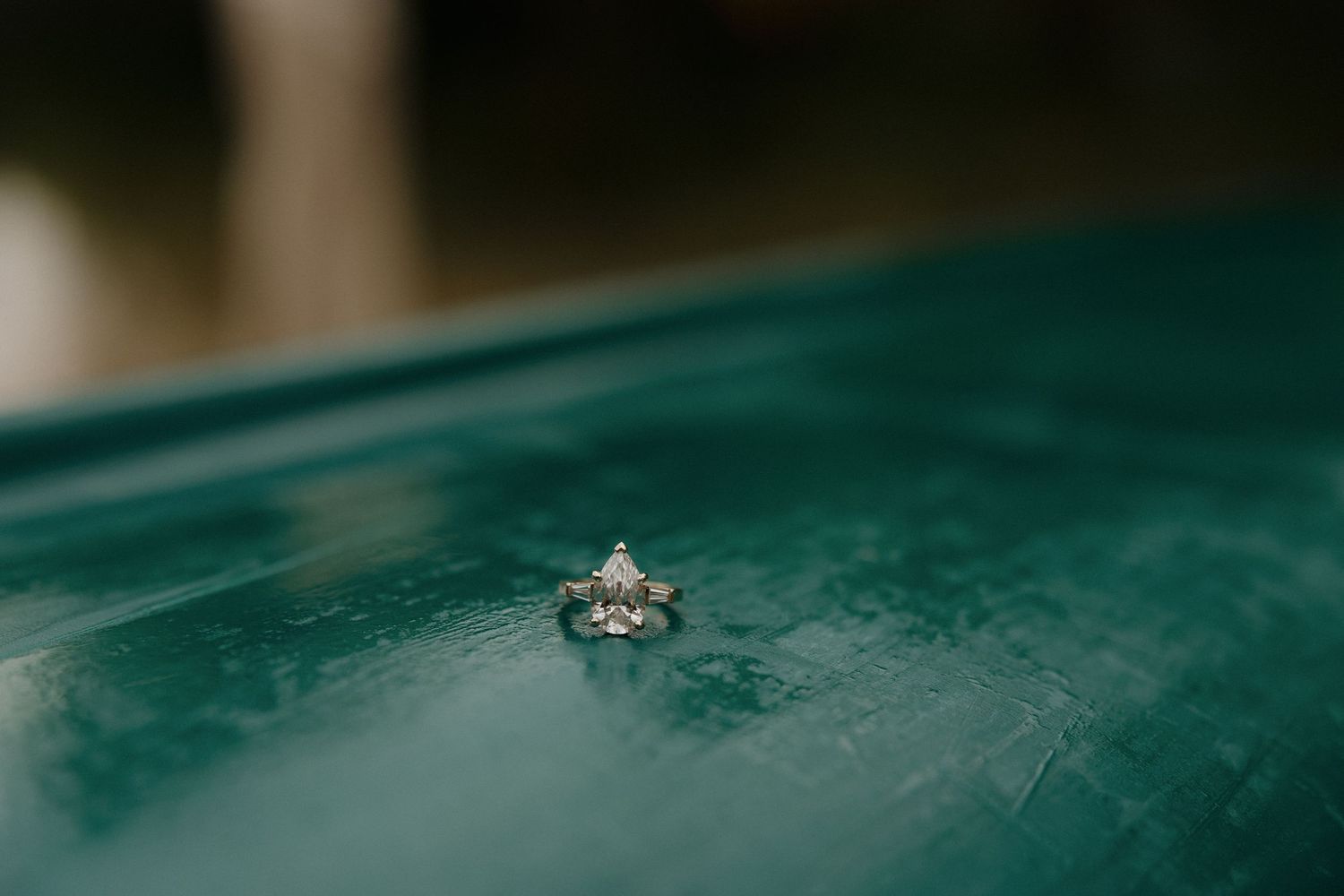 A sparkling engagement ring photographed against a teal-colored surface with water droplets.
