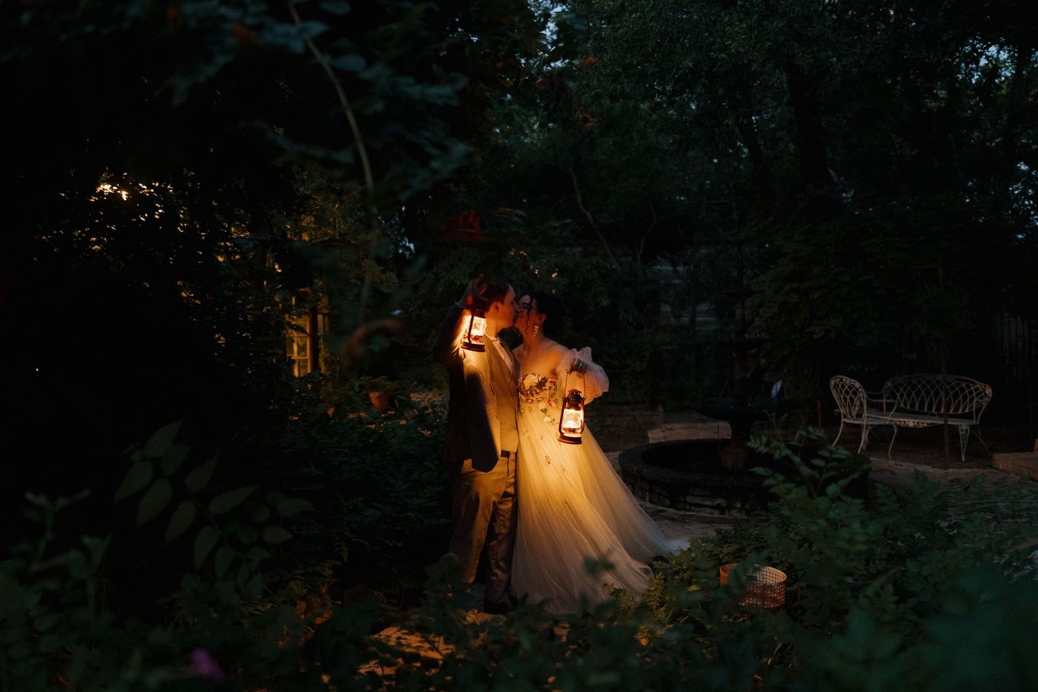 A dreamy nighttime scene with lantern light illuminating a flowing white dress in a garden setting.