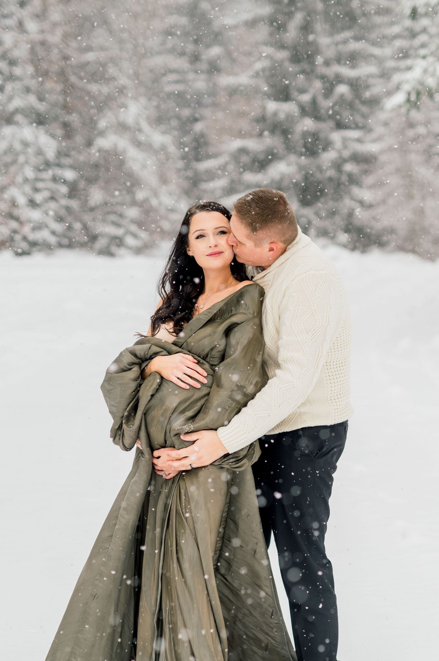 Couple standing in snowy forest in the mountains during an Idaho maternity session.