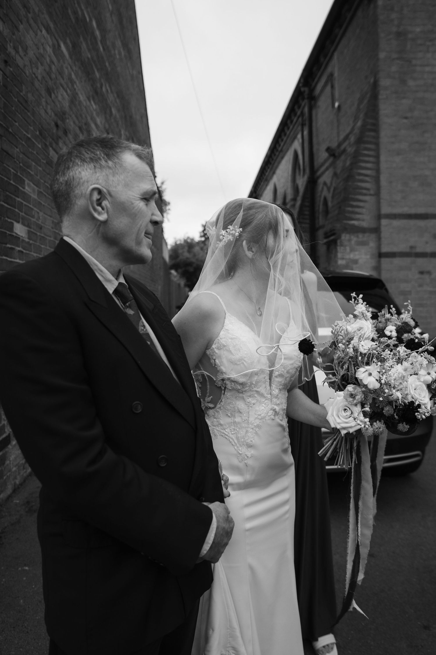 Black and white wedding portrait showing tender moments between newlyweds outside a brick building.