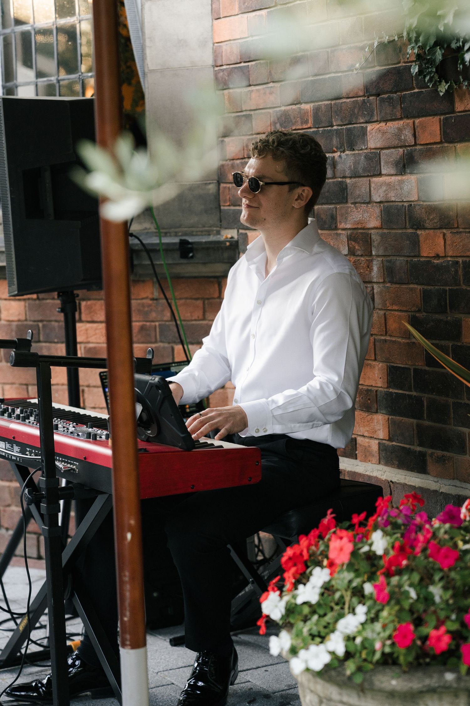 Musicians in white dress shirts perform at an outdoor venue with red and white flowers decorating the stage area.