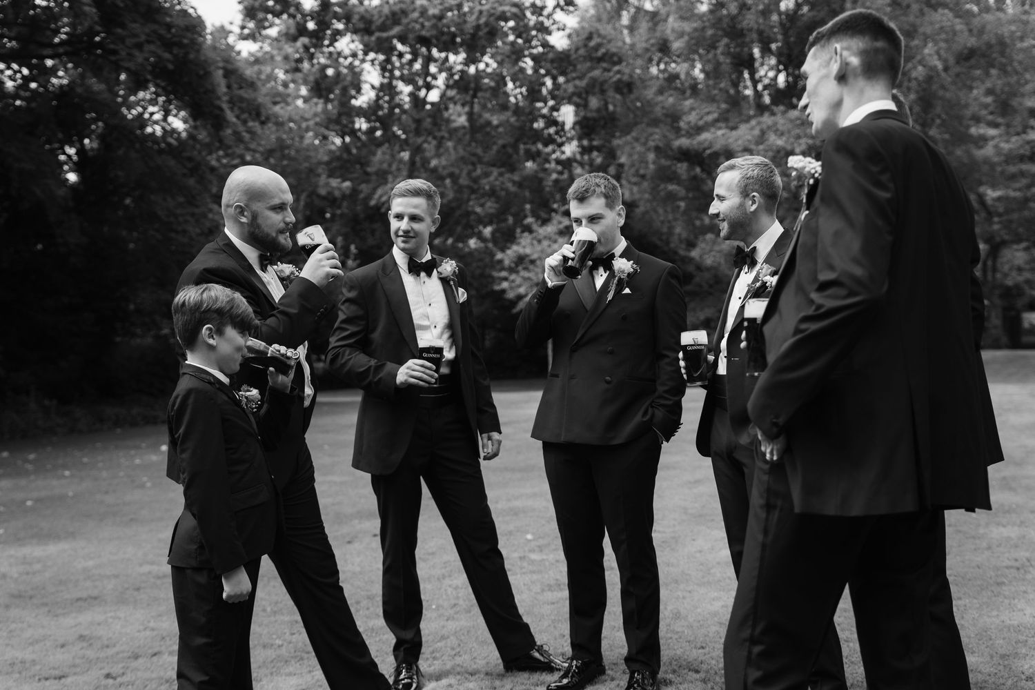 Wedding party in formal attire laughing together outdoors in a black and white photograph.