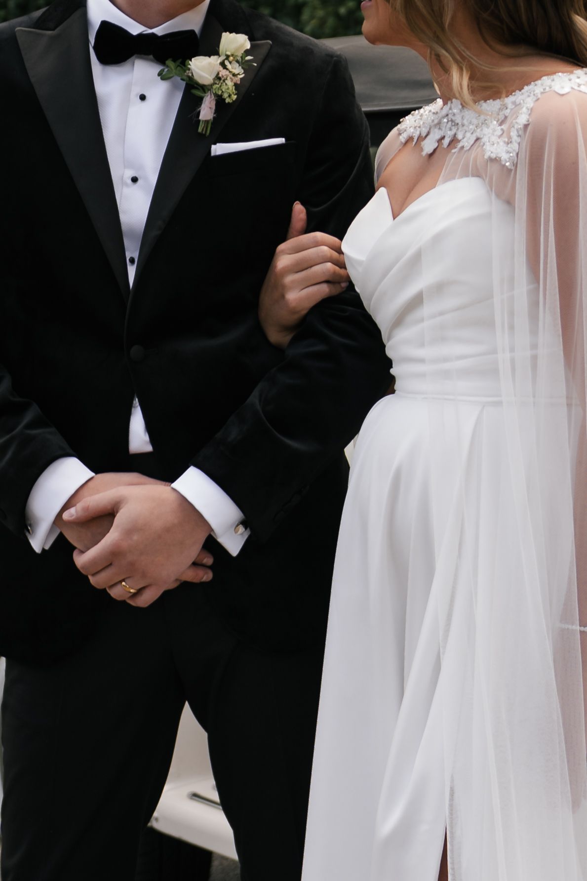 Close-up of bride in white lace dress and groom in black tuxedo with bowtie and boutonniere at wedding ceremony.