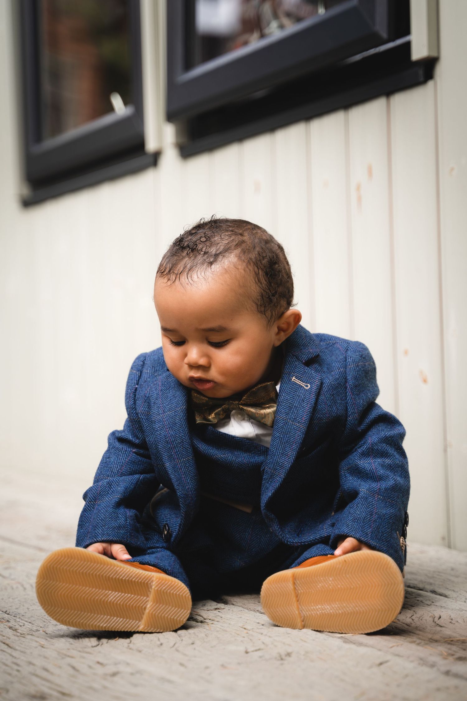 A toddler in a navy blue blazer curiously peers under a door in a sequence of playful photos.