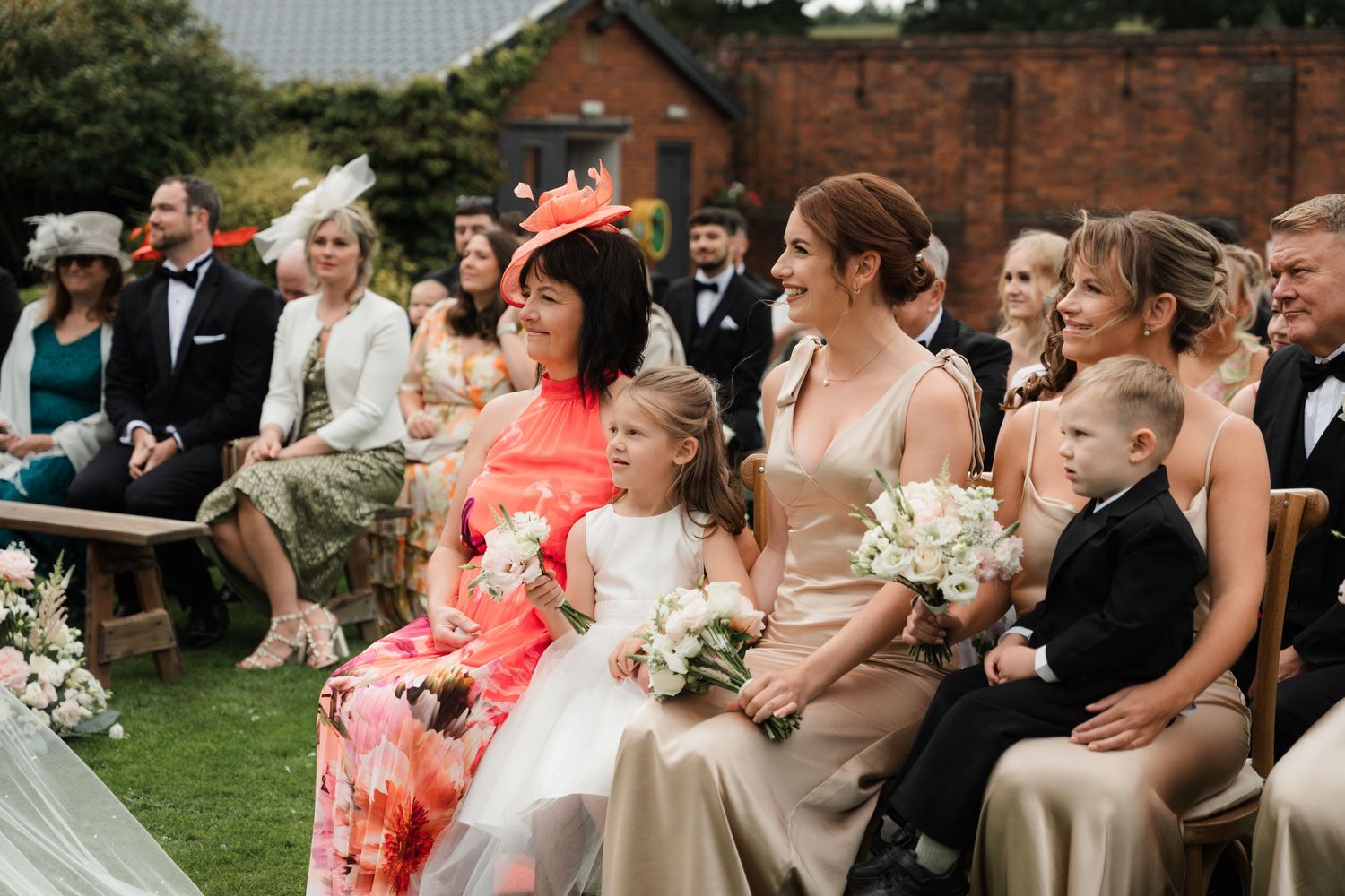 Wedding guests seated outdoors in rows watch an emotional ceremony moment during a summer celebration.