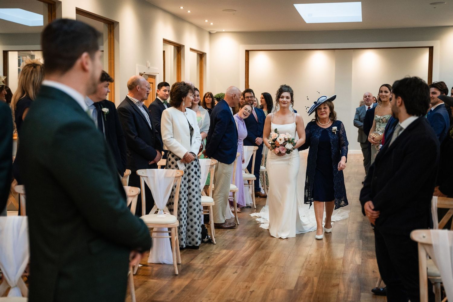 Wedding guests mingle and socialize in an elegant indoor venue with white walls and hardwood floors.