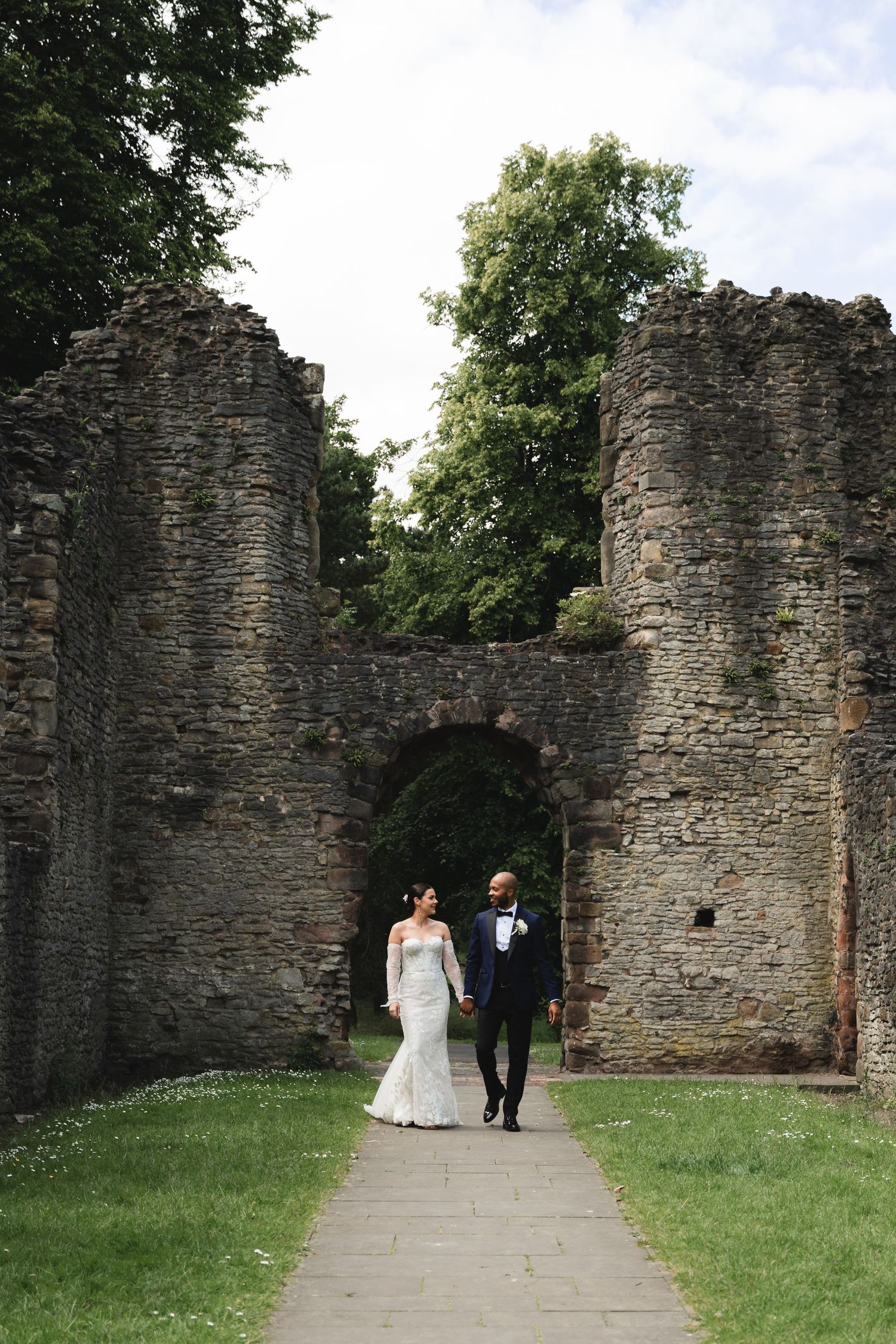 Couple walks through ancient stone archway ruins during wedding photoshoot.