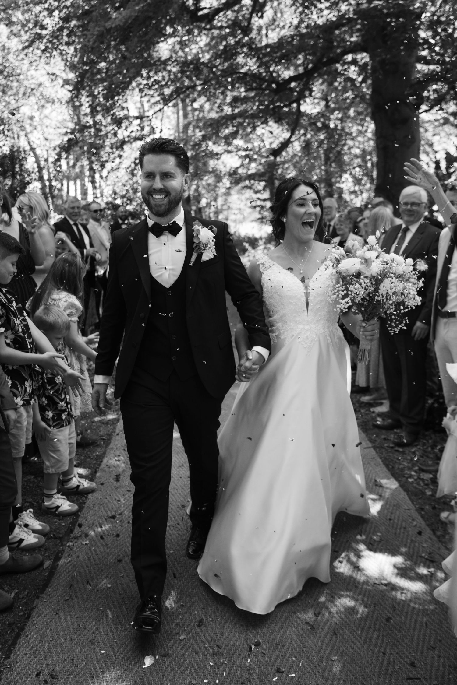 Wedding party walking through shower of confetti on brick pathway.