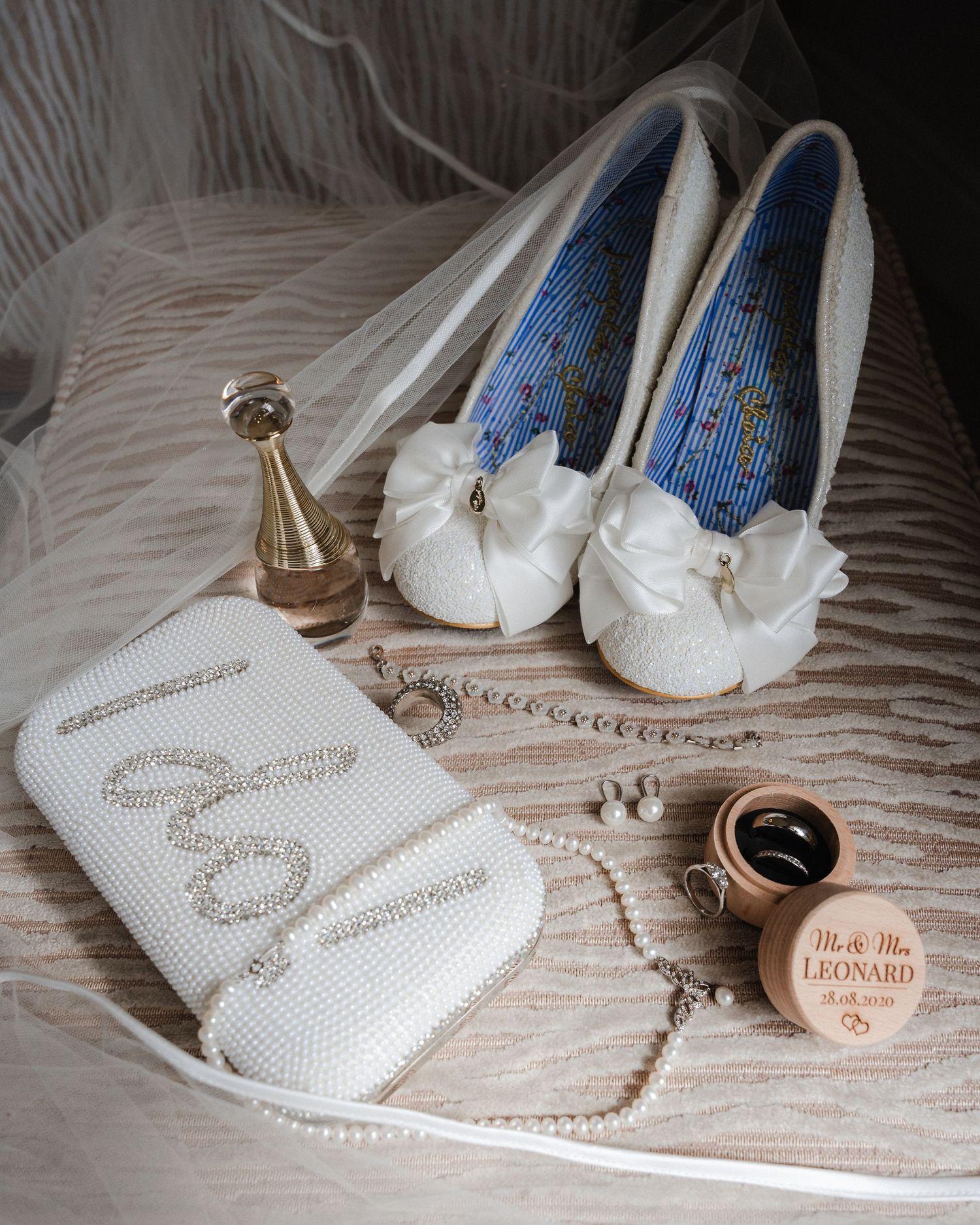 Elegant white bridal shoes with blue embroidery detail and perfume bottles arranged on textured fabric.