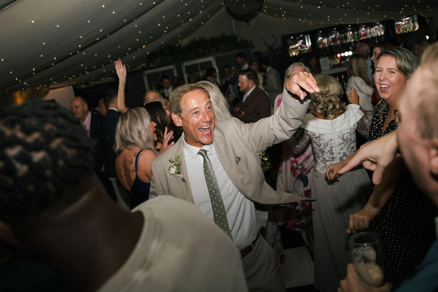 Wedding guests dance and celebrate together on a dimly lit dance floor at a reception party.