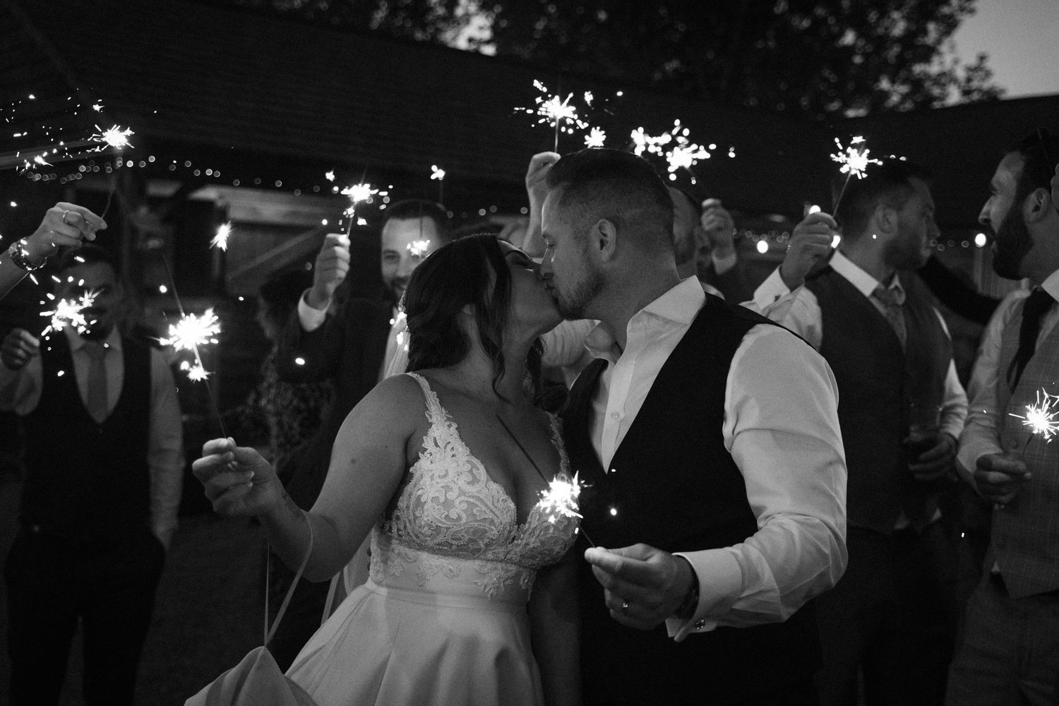 Wedding guests dance with sparklers at night during an outdoor celebration creating magical light trails in the darkness.