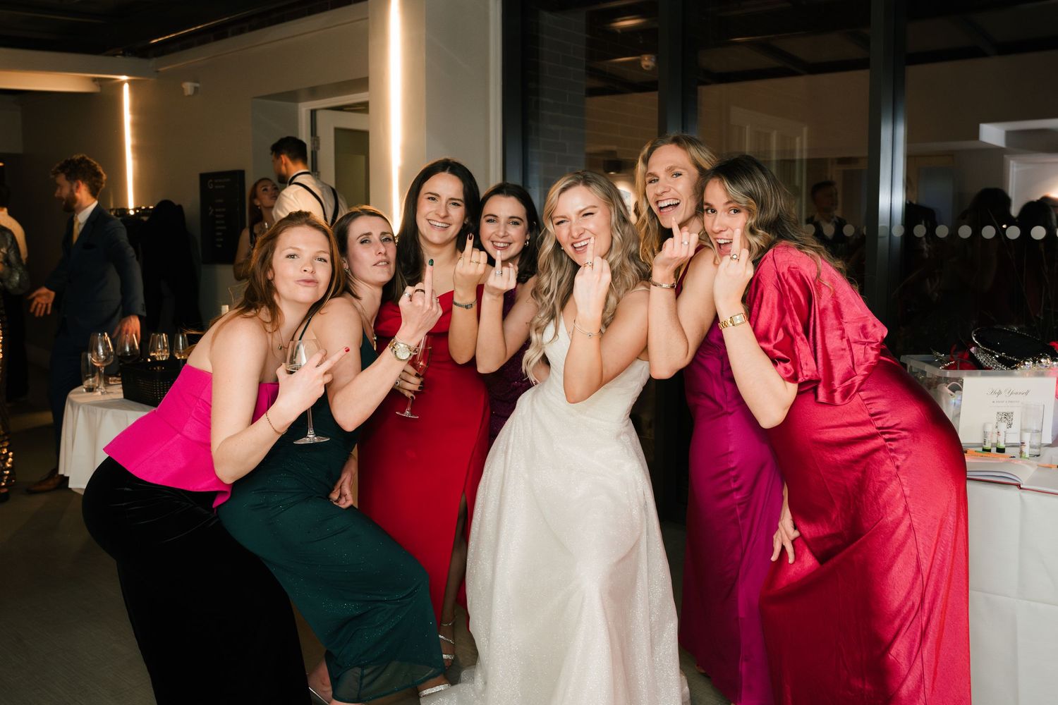 A group of wedding party members in red and green dresses dance together at a celebration.