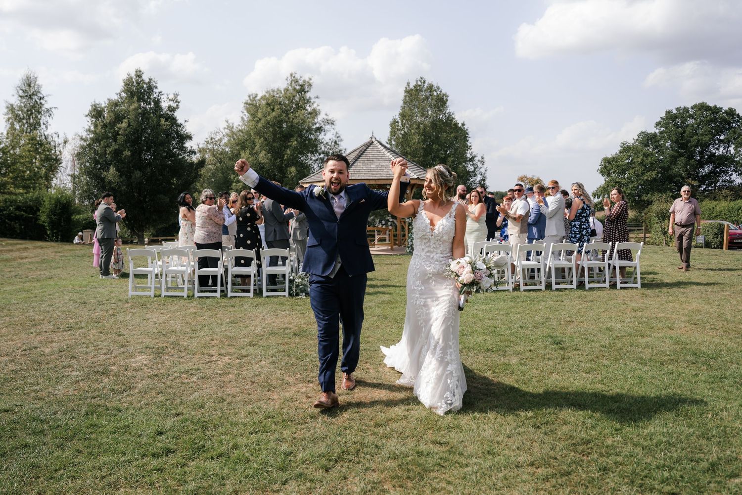 Wedding guests gather on a grassy hillside for an outdoor celebration on a sunny afternoon.
