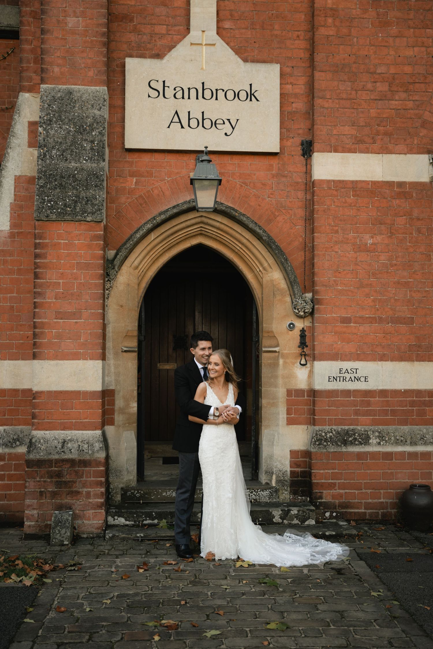 Bride and groom share romantic moments in front of red brick church entrance at Stanbrook Abbey.