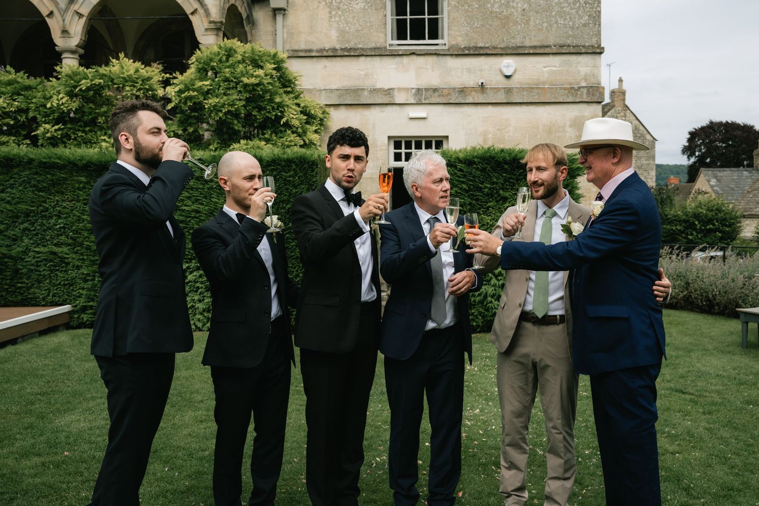 Groomsmen and guests gather outdoors at a formal garden wedding celebration.