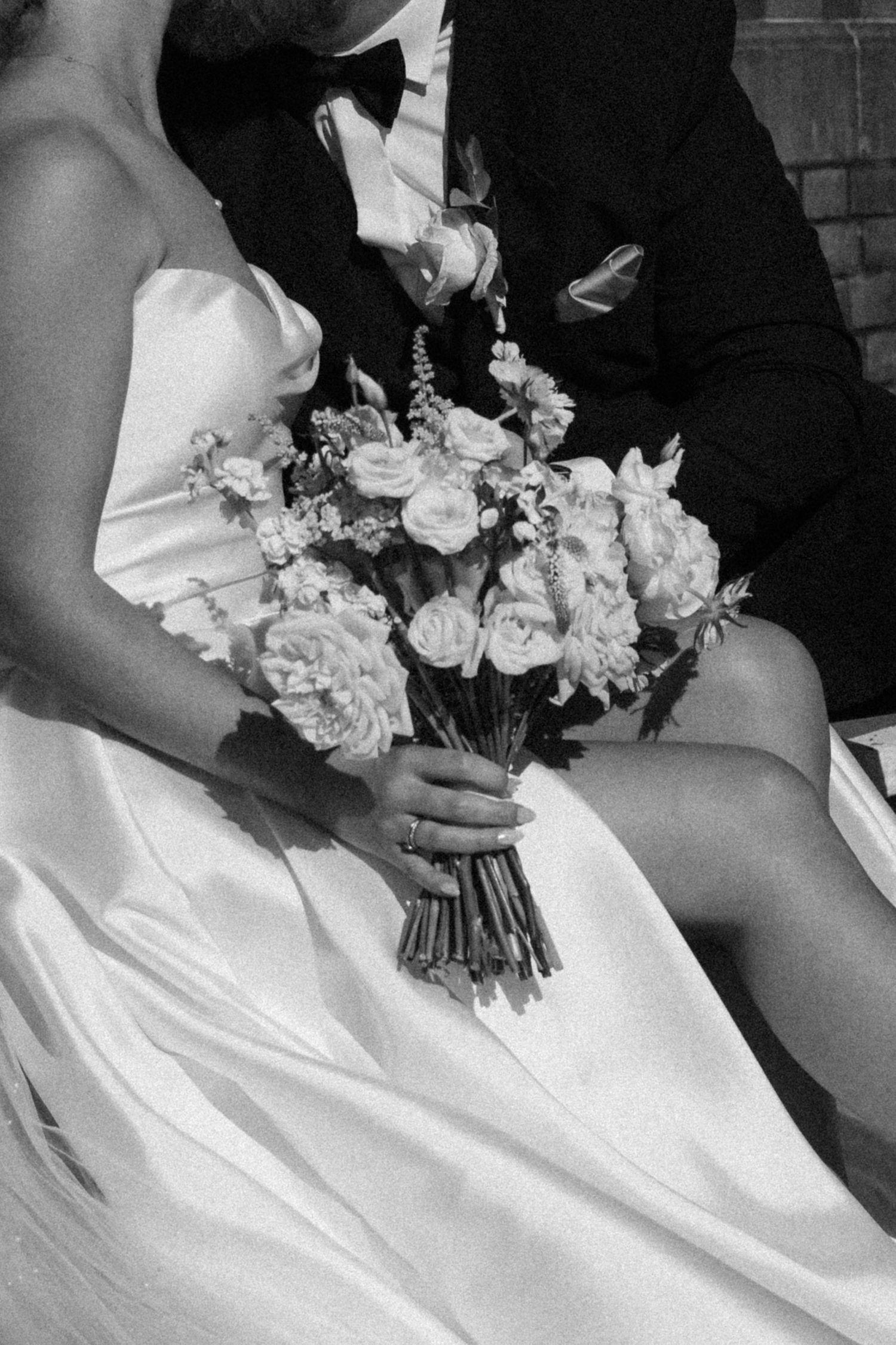 A row of bridesmaids in black dresses hold elegant white floral bouquets against their white gowns.