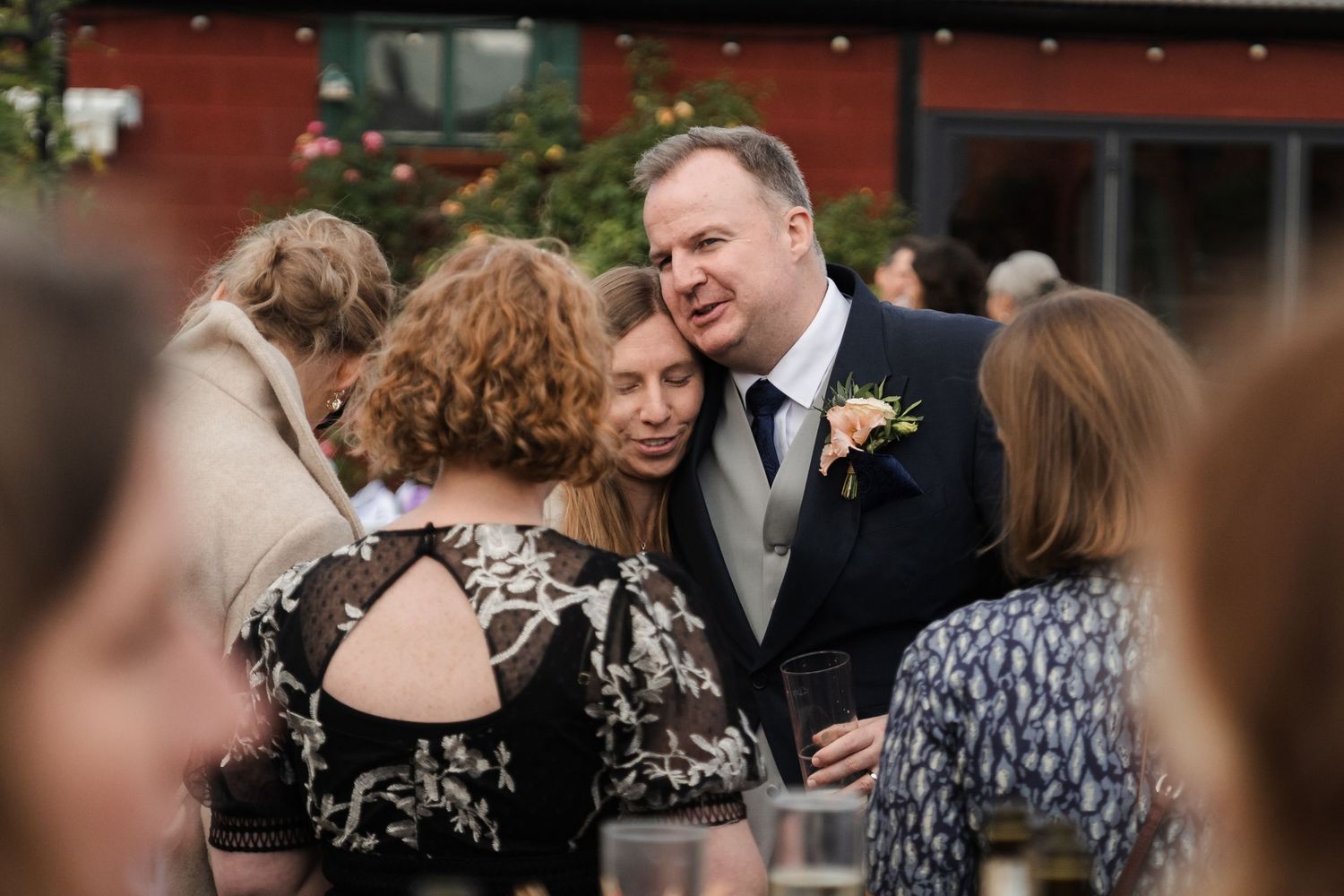 A group of wedding guests dancing and celebrating together at an indoor reception venue with red walls.