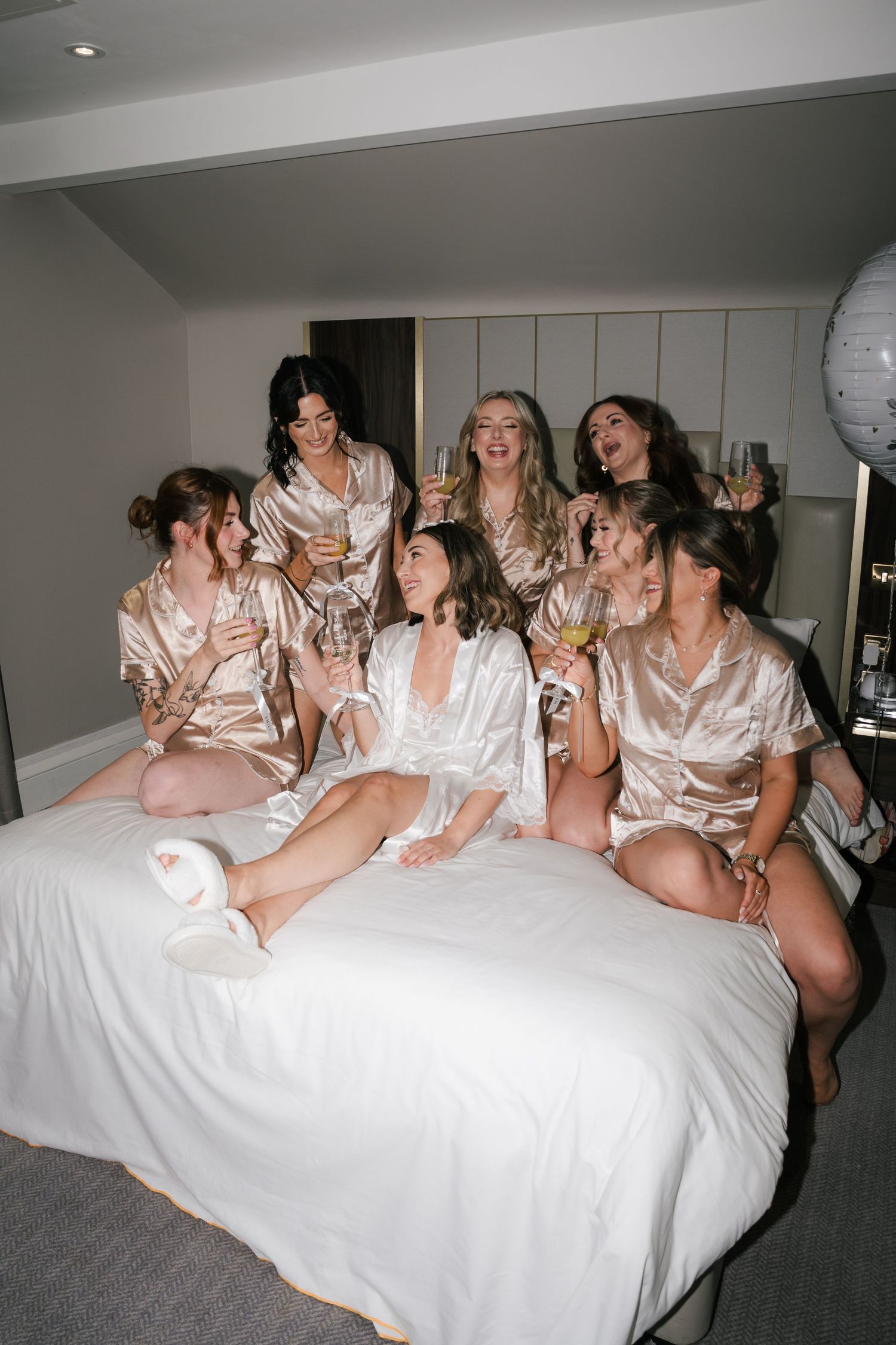 A group of women in satin robes having fun posing together on a white bed during a special celebration.