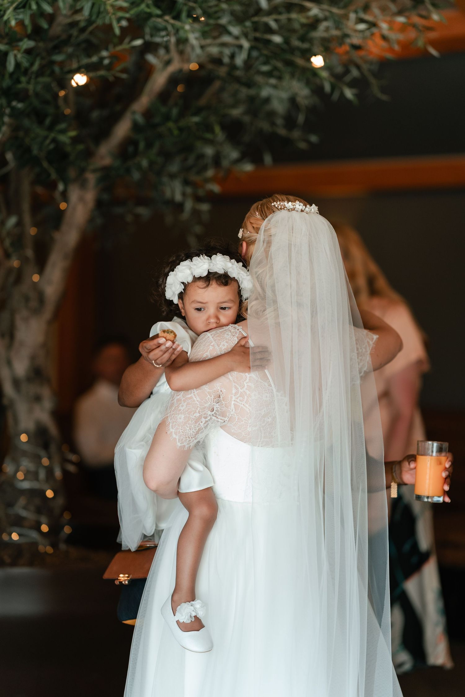 A tender moment at a wedding reception with a flowing white veil and delicate floral crown in an intimate setting.
