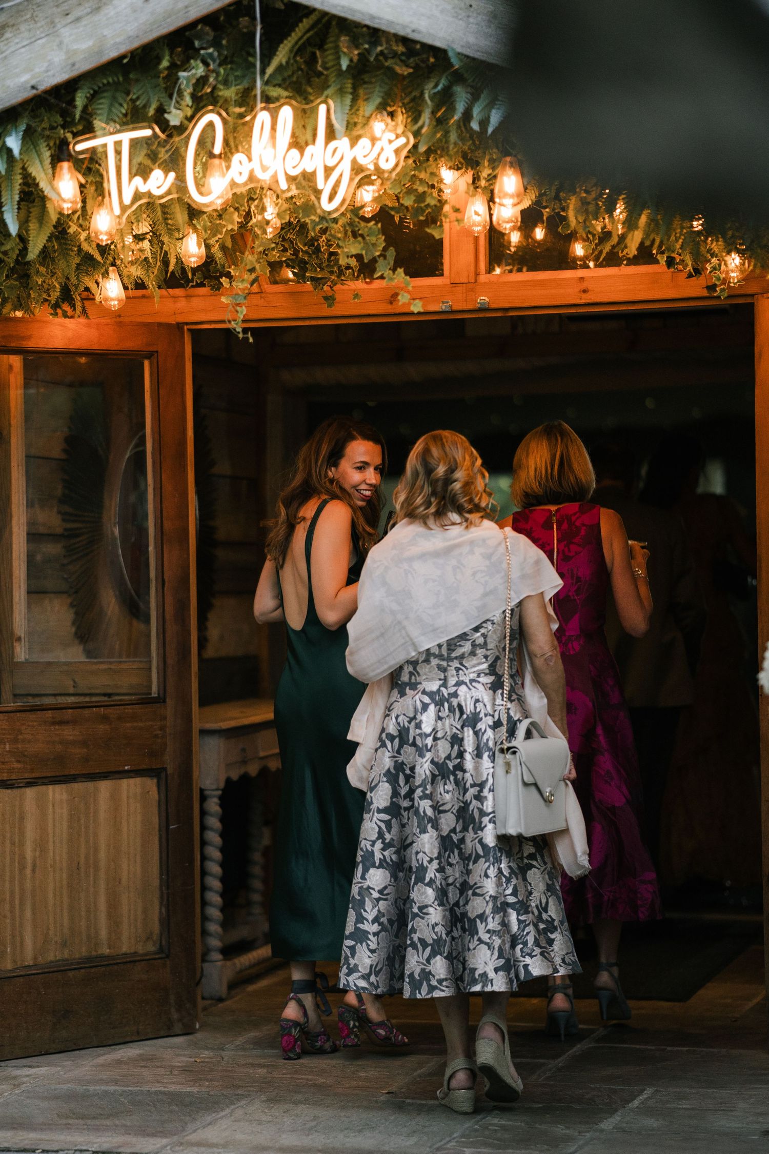 Guests gather at a rustic wooden venue with warm lighting and holiday greenery decorations overhead.