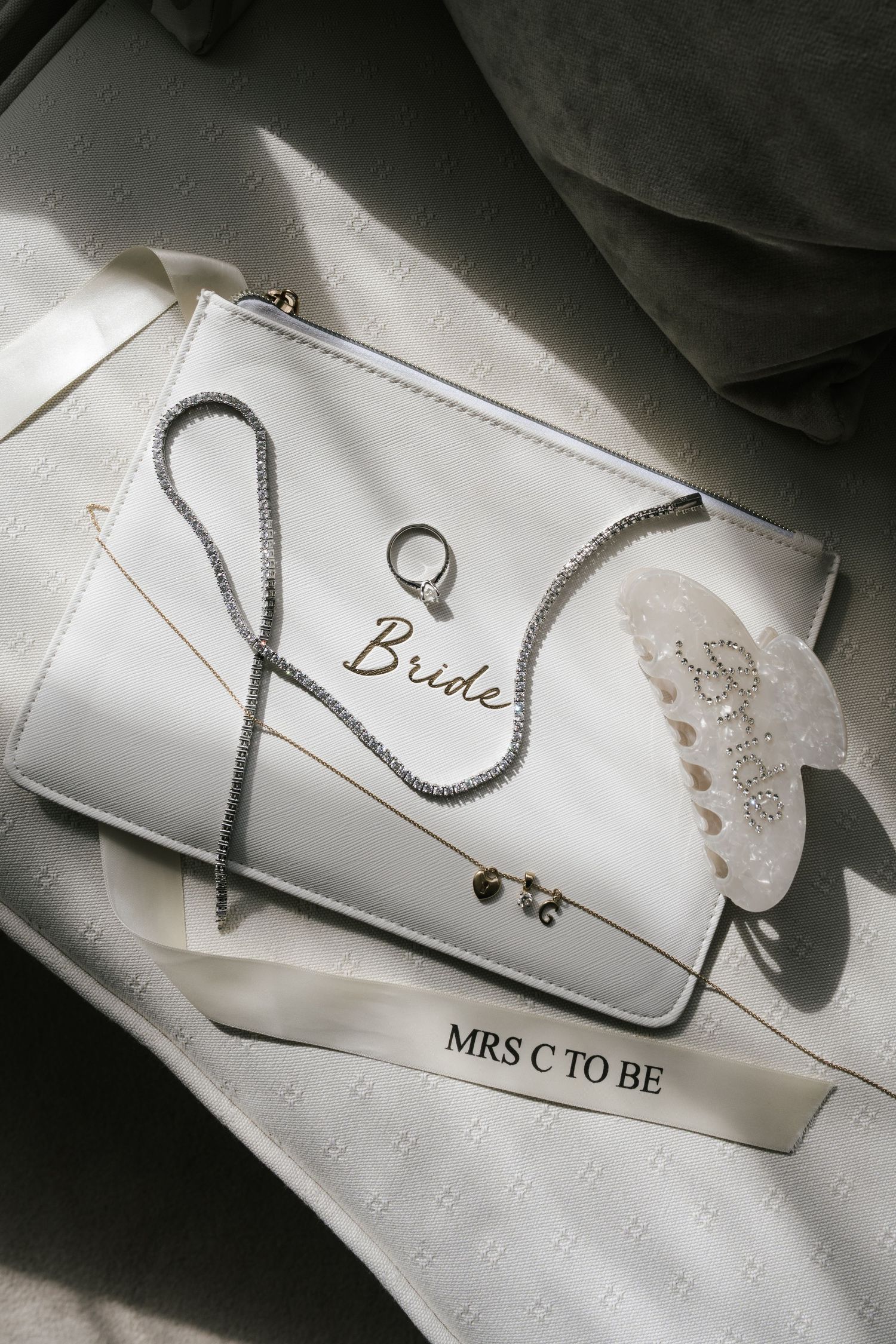Wedding stationery and jewelry details including name cards and rings arranged on white textured surface in monochromatic style.