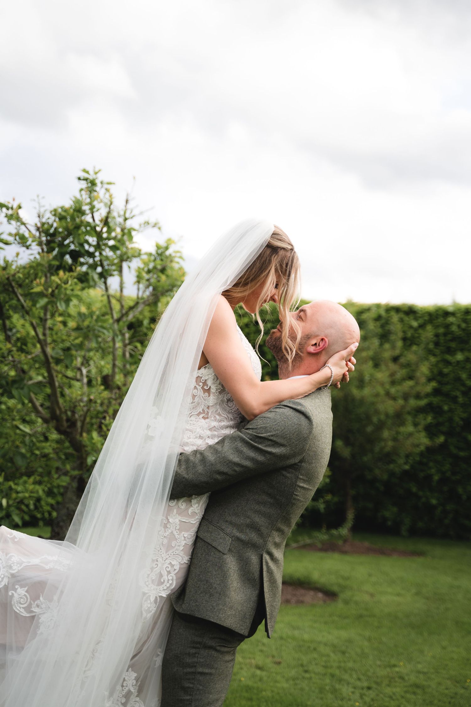 A joyful wedding moment captured outdoors as a couple embraces in a garden setting with lush greenery.