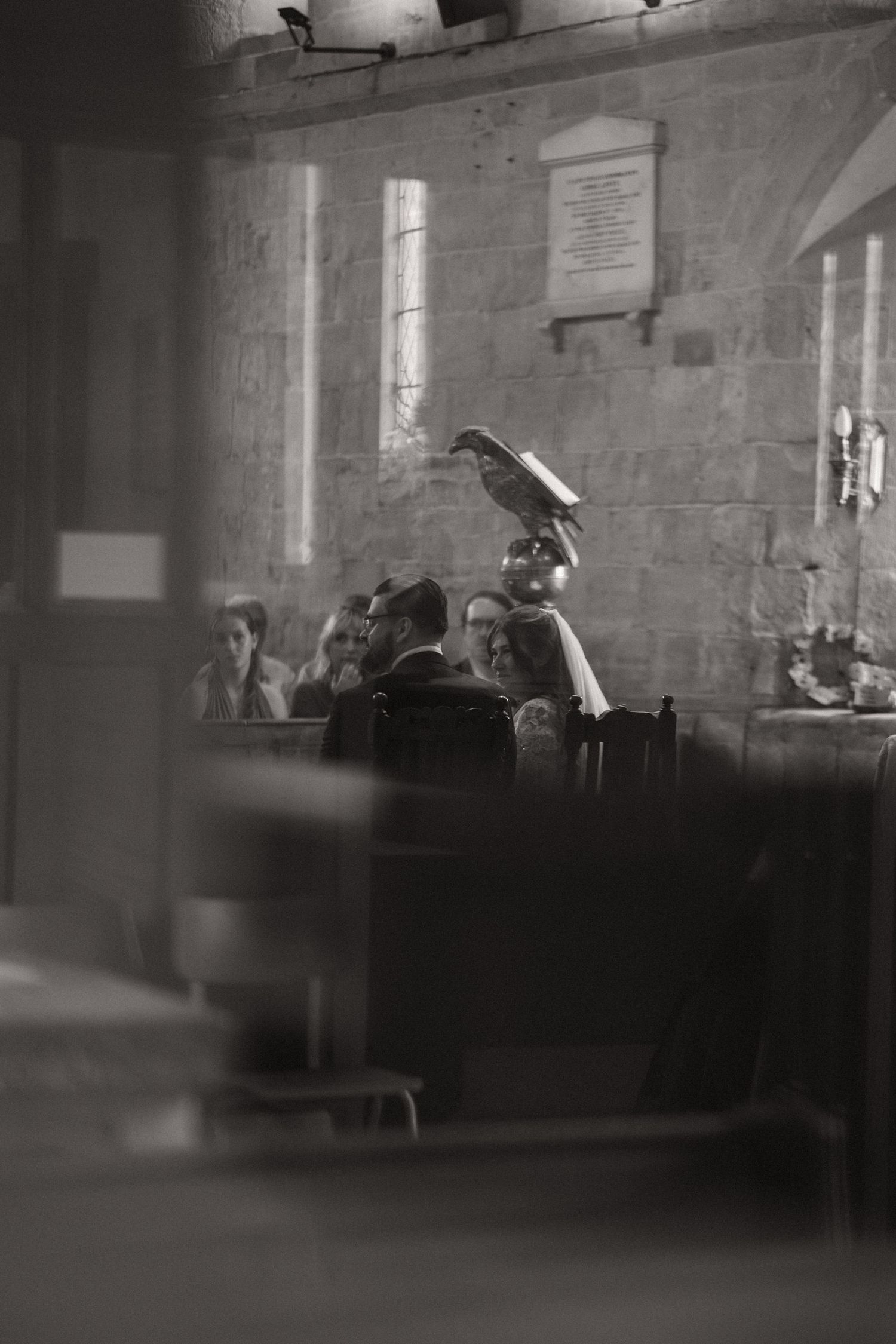Black and white photograph showing students in a classroom with sunlight streaming through windows onto stone walls.