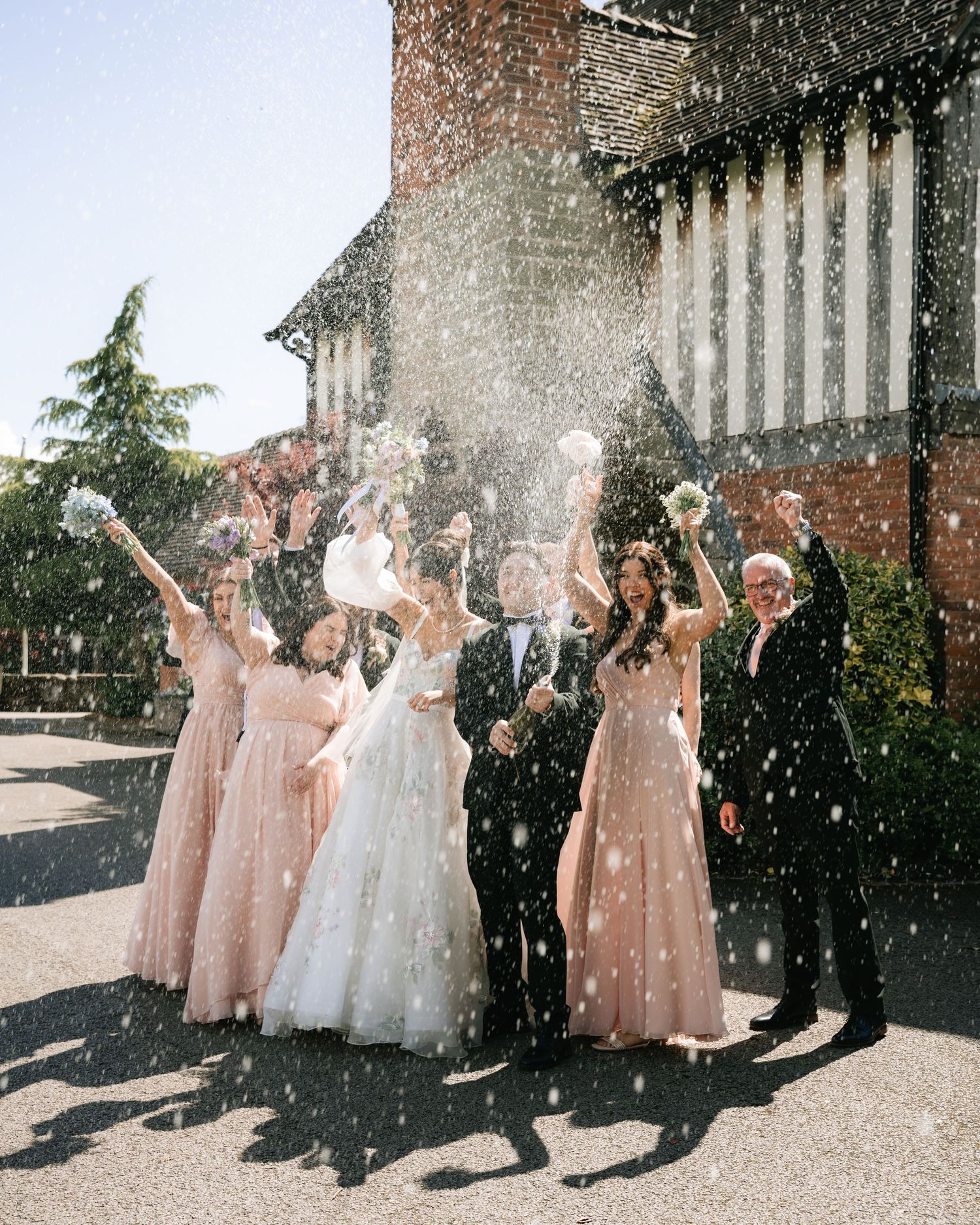 Wedding party in pink dresses celebrating with confetti in bright sunlight.
