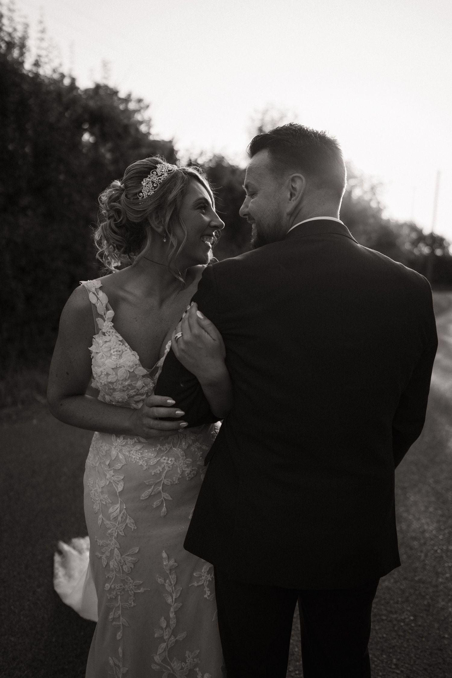 A romantic black and white wedding photo shows a couple sharing an intimate moment outdoors at sunset.