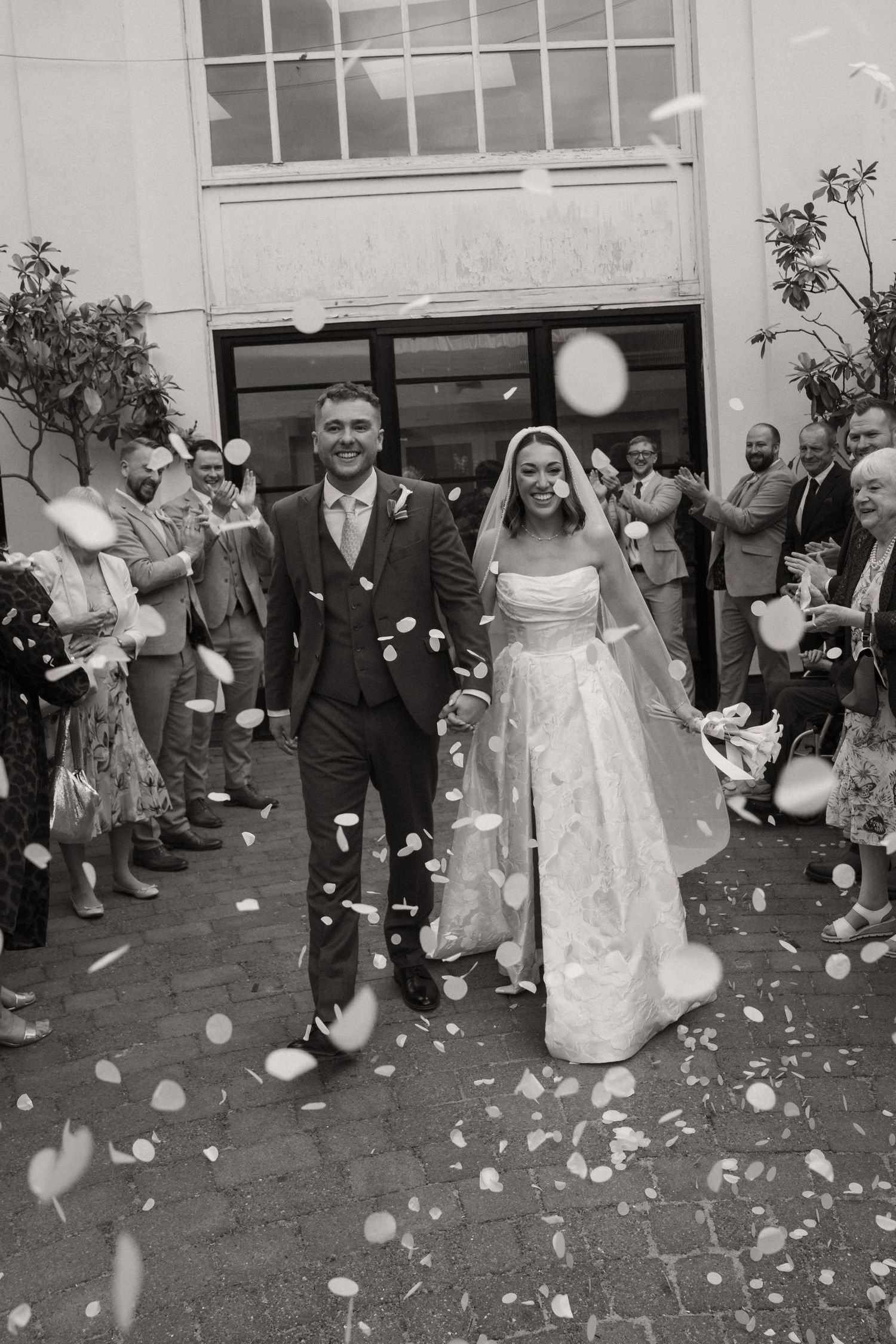 Black and white sequence of wedding guests throwing flower petals at a couple exiting a church building.