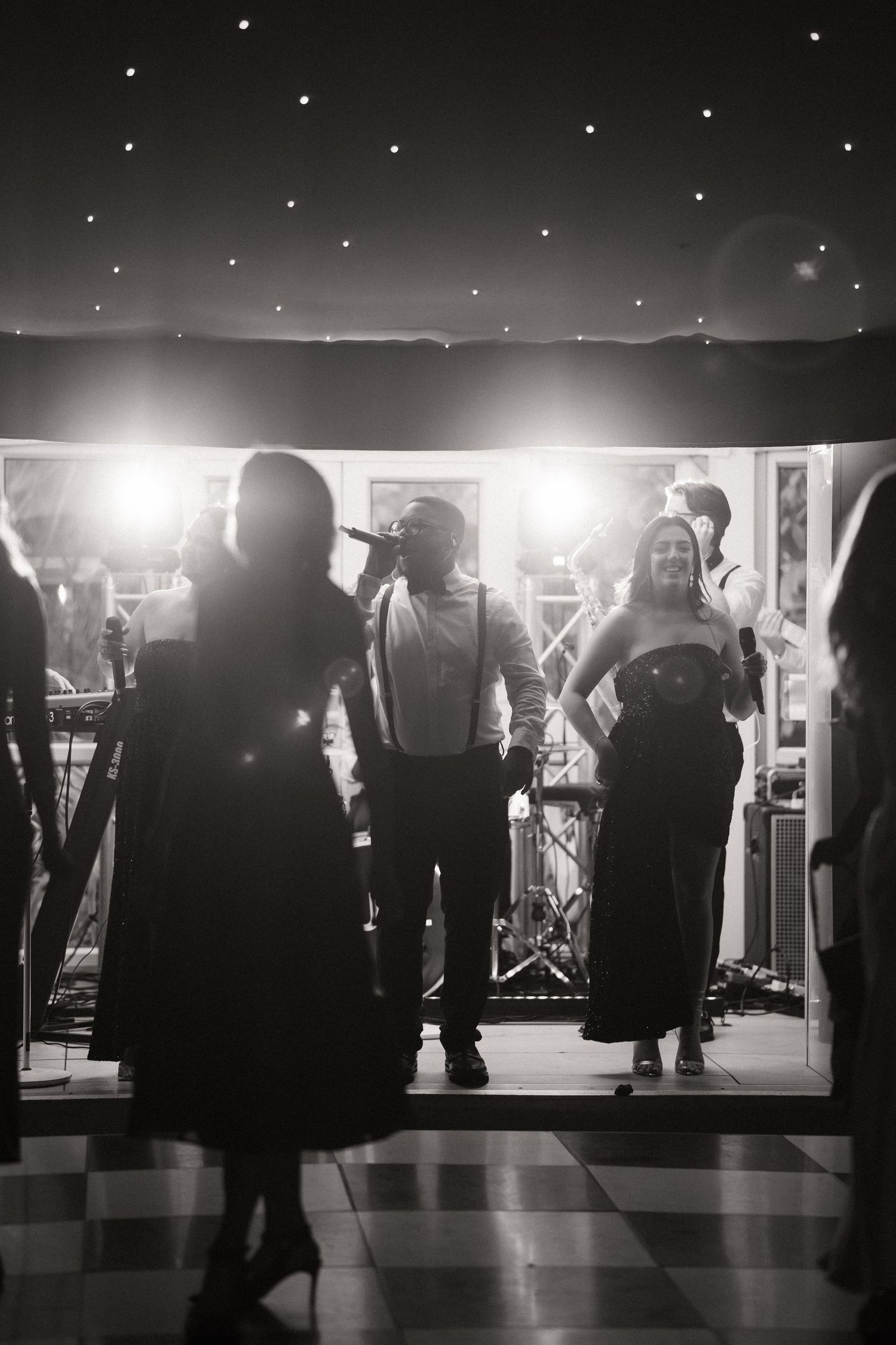 Silhouettes of people dancing under starlit night sky at an outdoor venue with bright spotlights.