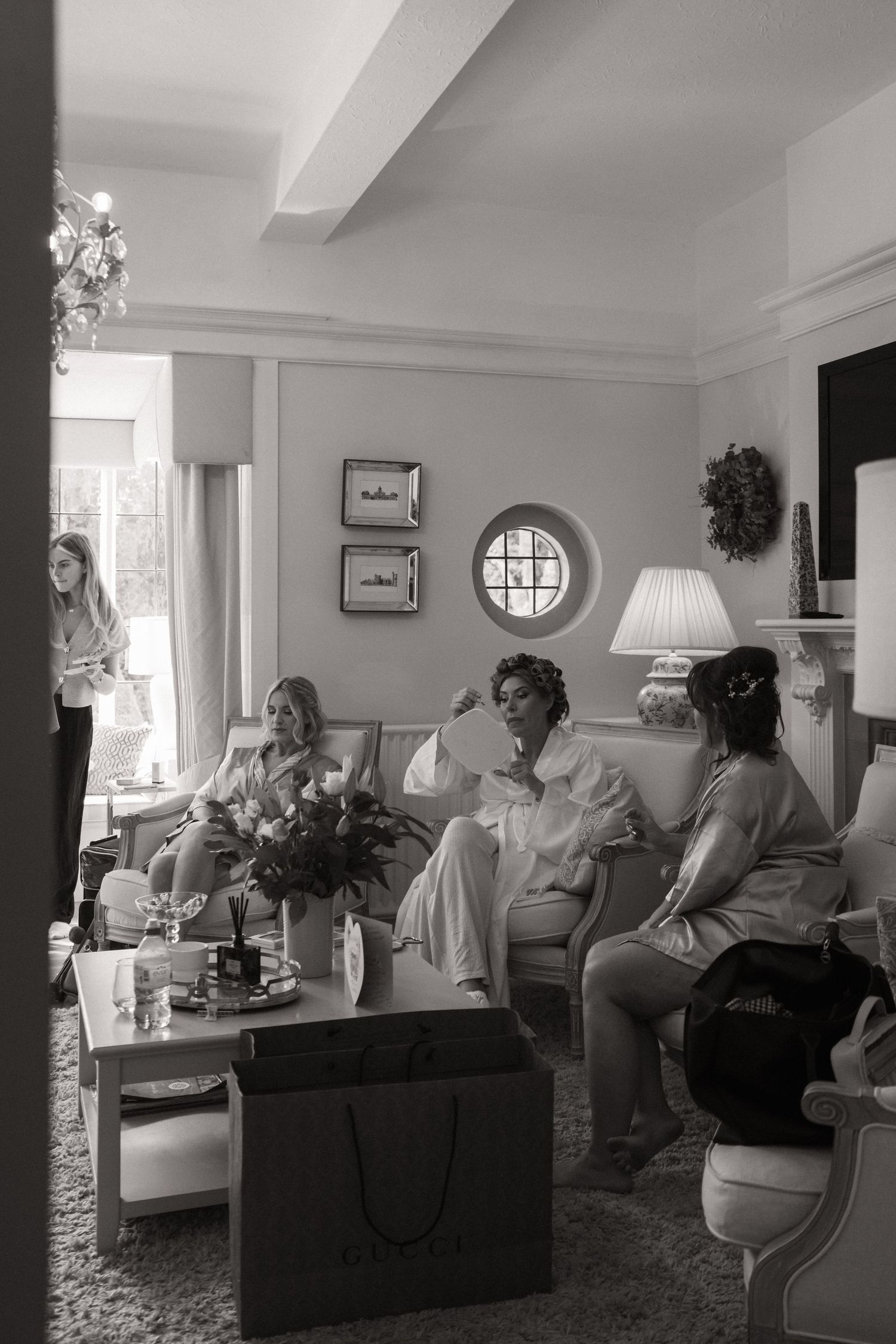 Black and white photograph of people relaxing in an elegant lounge area with plush seating and round window details.