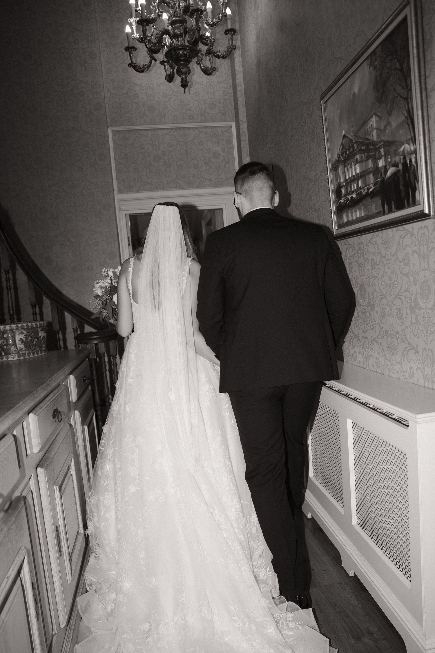 A black and white photo series showing a bride in a flowing white wedding gown walking up stairs with her escort.
