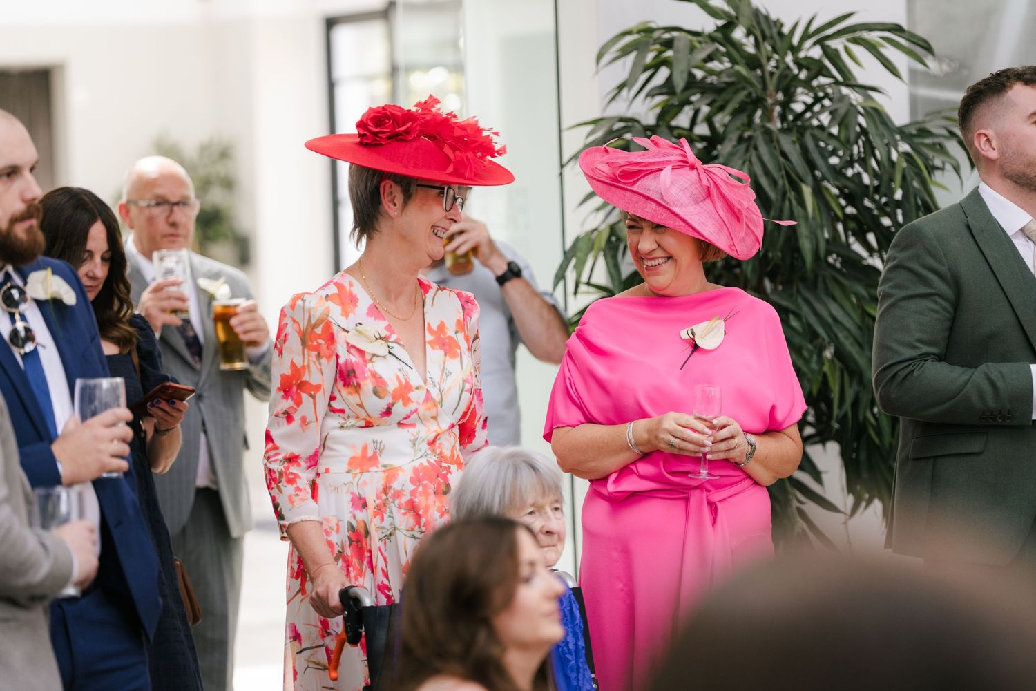 Wedding guests in bright pink and floral outfits mingle during a celebration at an indoor venue.