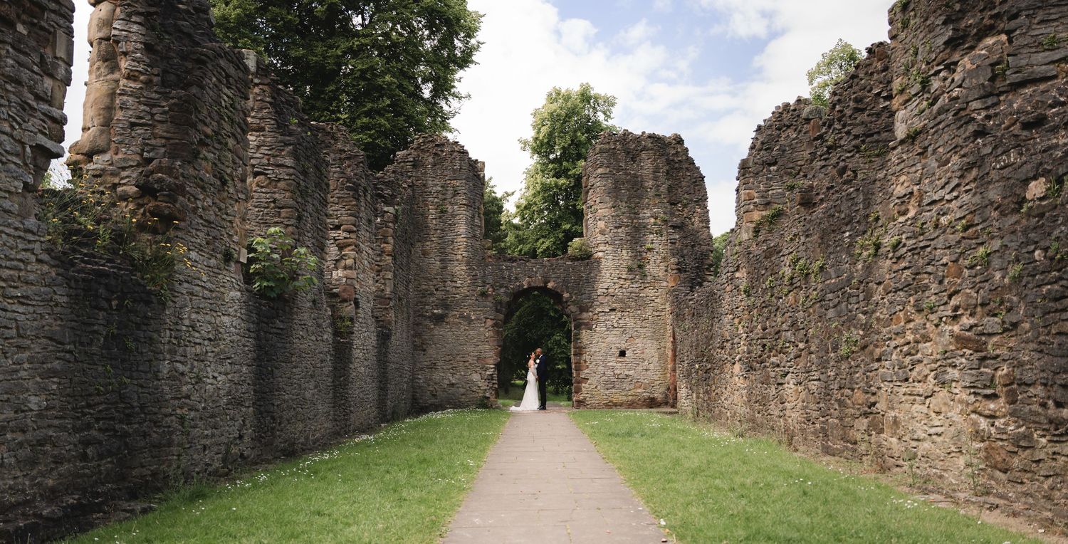 Stone ruins of an ancient castle with grassy path leading through arched doorway in Wales.
