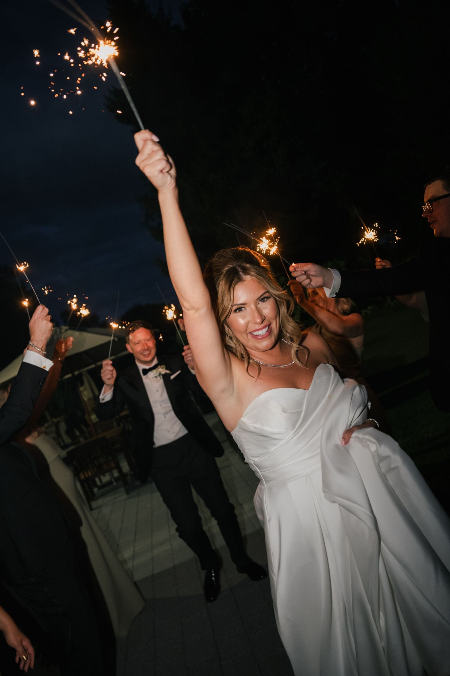 Wedding celebration at night with sparklers creating a festive atmosphere as guests celebrate outside.