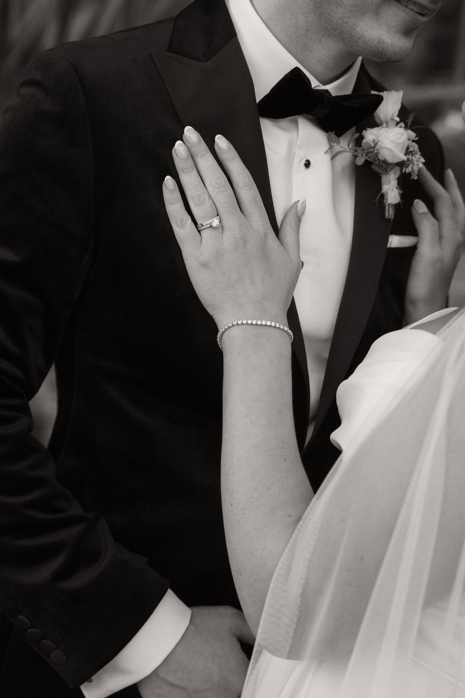 Close-up black and white photo of newlyweds wearing formal wedding attire and pearl jewelry.