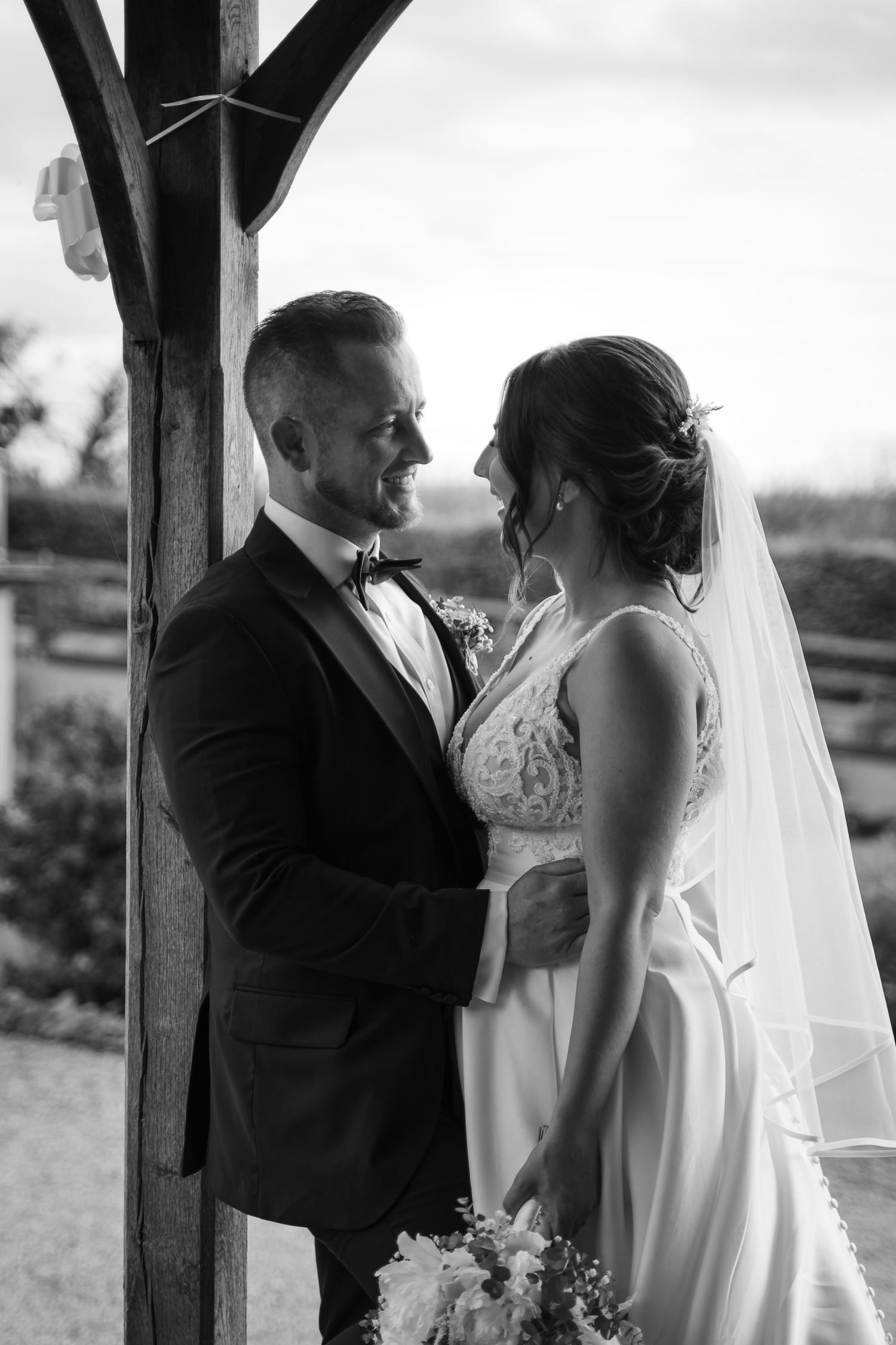 A romantic black and white wedding photo series showing tender moments between newlyweds under a rustic wooden structure.
