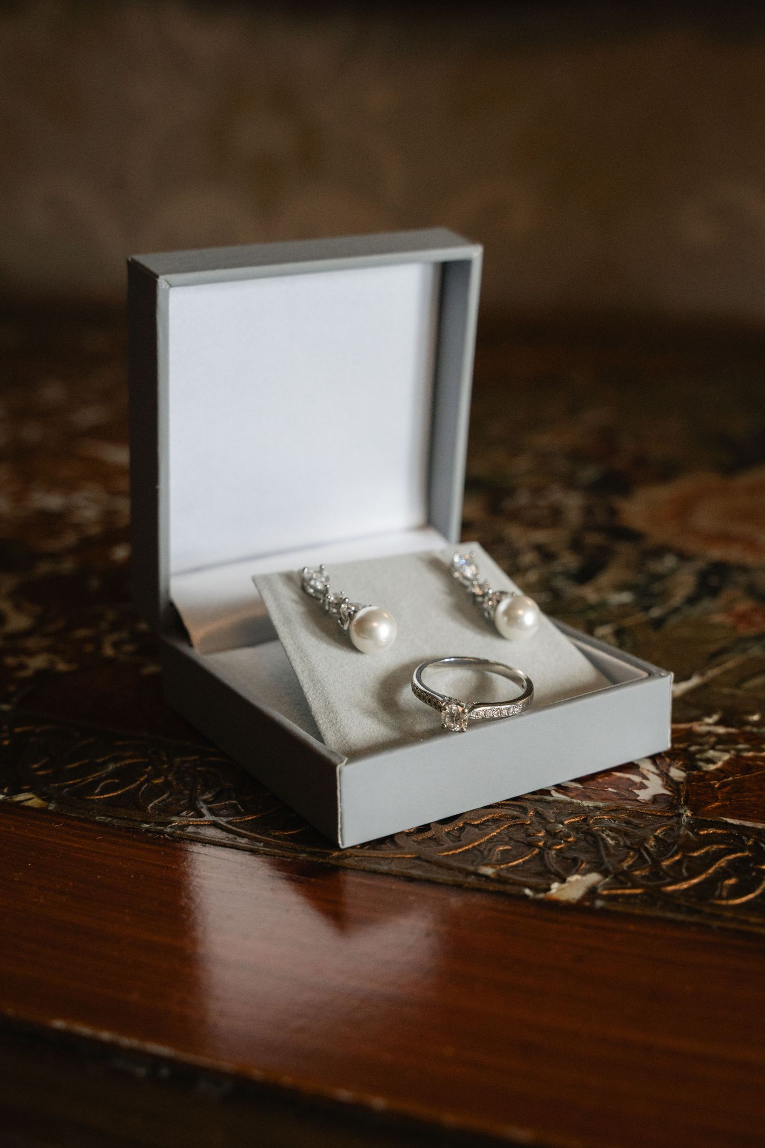 A white jewelry box containing delicate rings and accessories photographed in a sequence on a dark wooden surface.