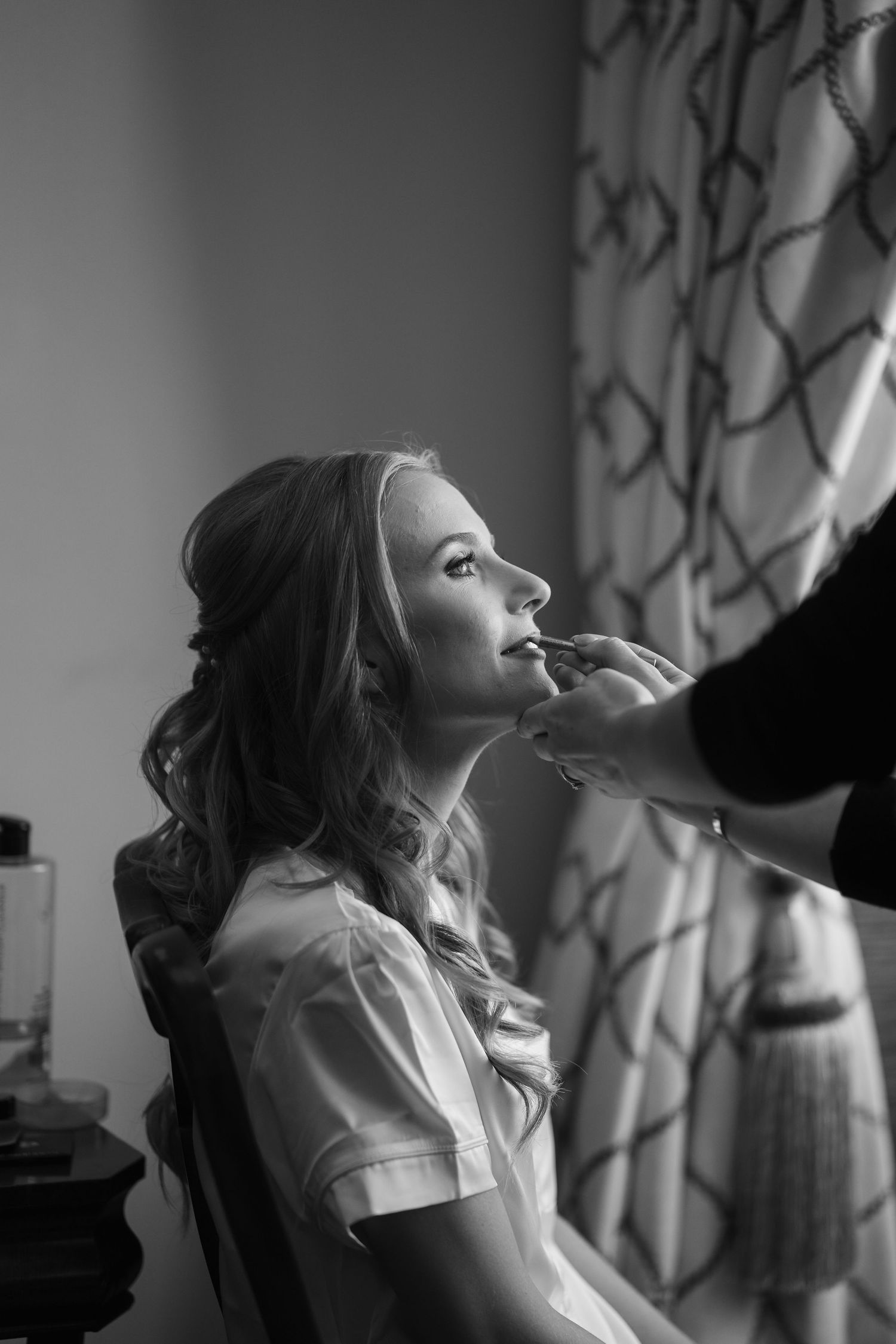A sequence of black and white photos showing someone getting makeup applied while wearing a white top.
