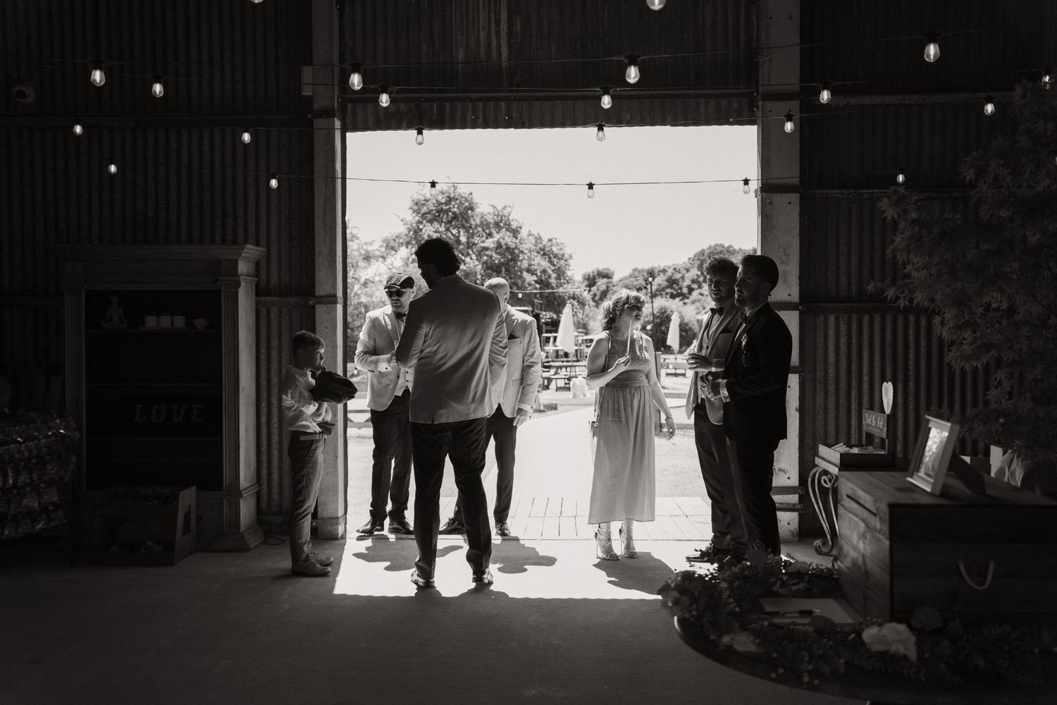 A black and white wedding photo capturing silhouettes of people standing in a bright doorway entrance.