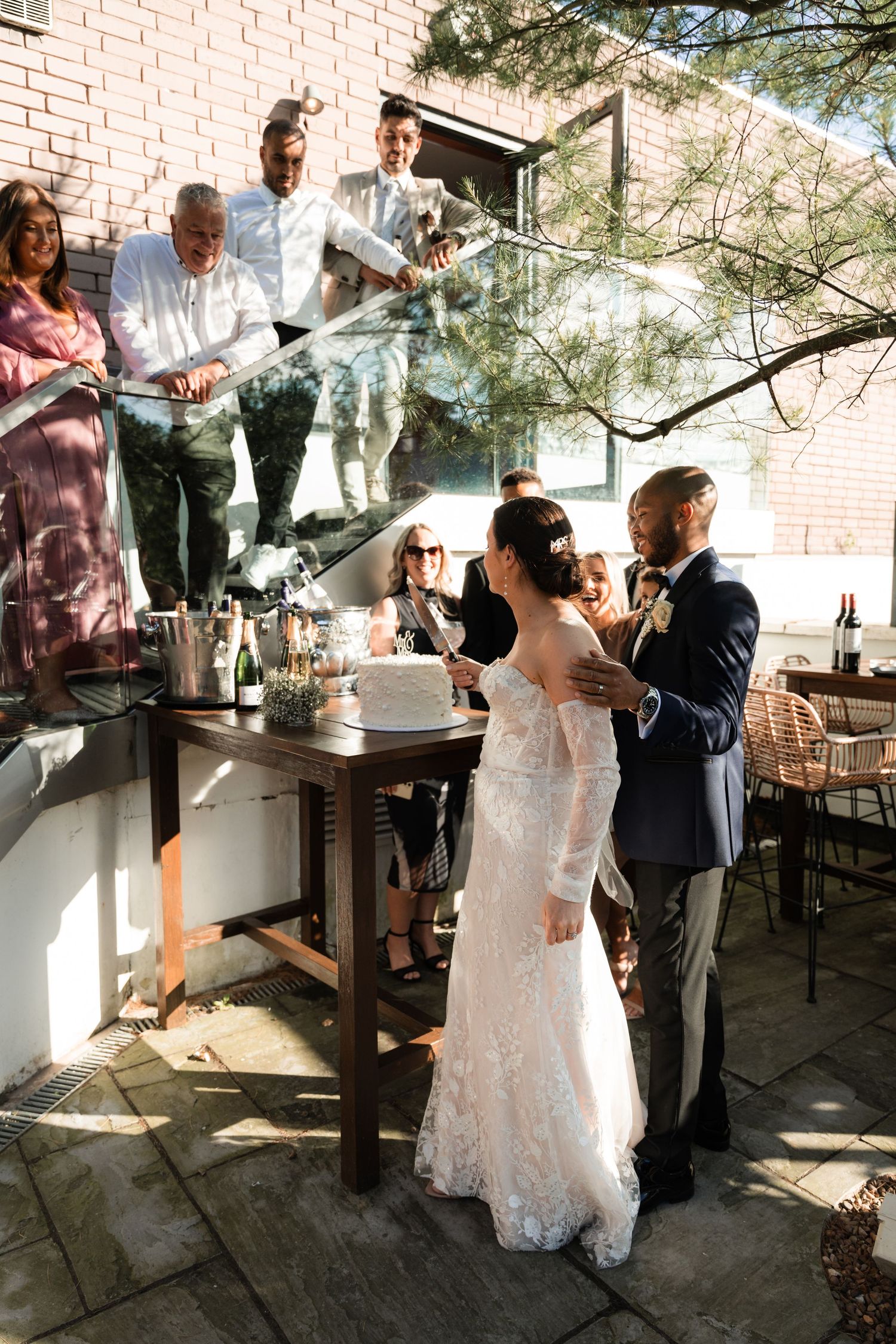 A couple dances together on an outdoor patio surrounded by brick walls and trees in natural lighting.