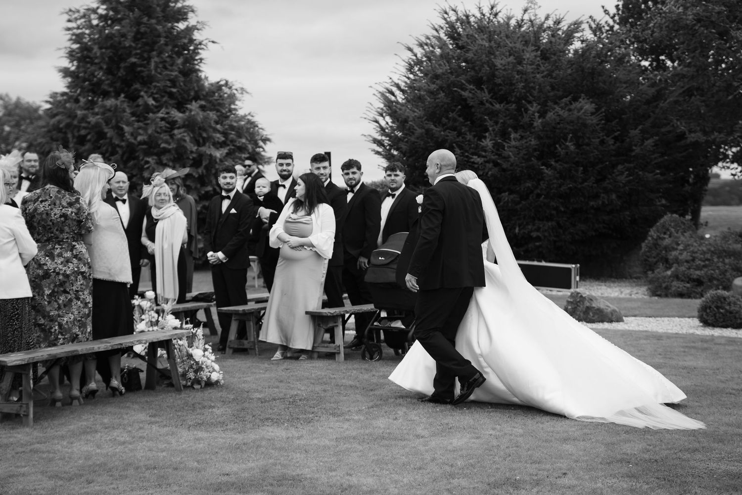 A series of black and white wedding photos showing outdoor garden scenes with guests and a flowing white dress.
