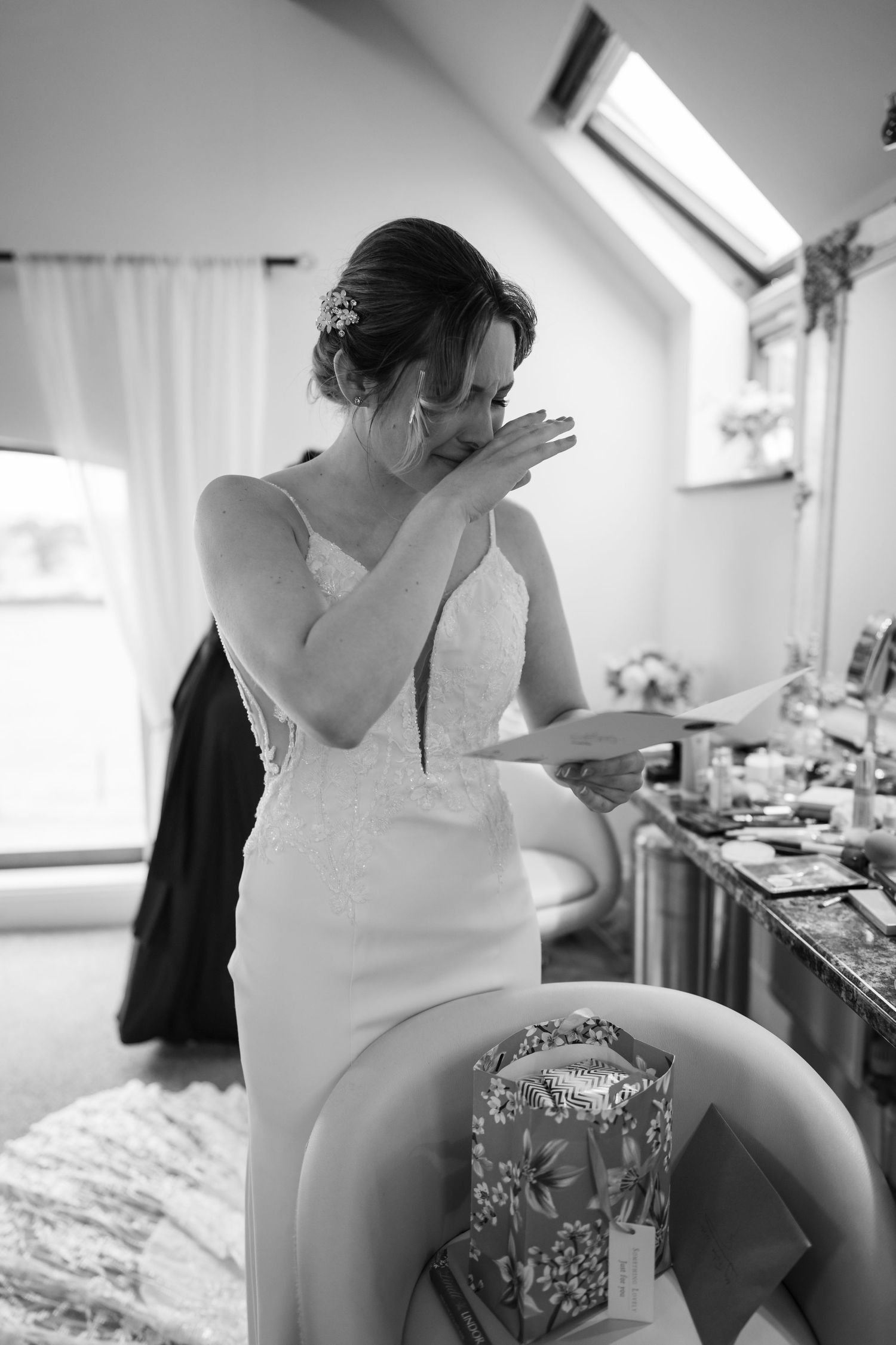 Black and white photograph of a bride getting ready in a sunlit room with white curtains.