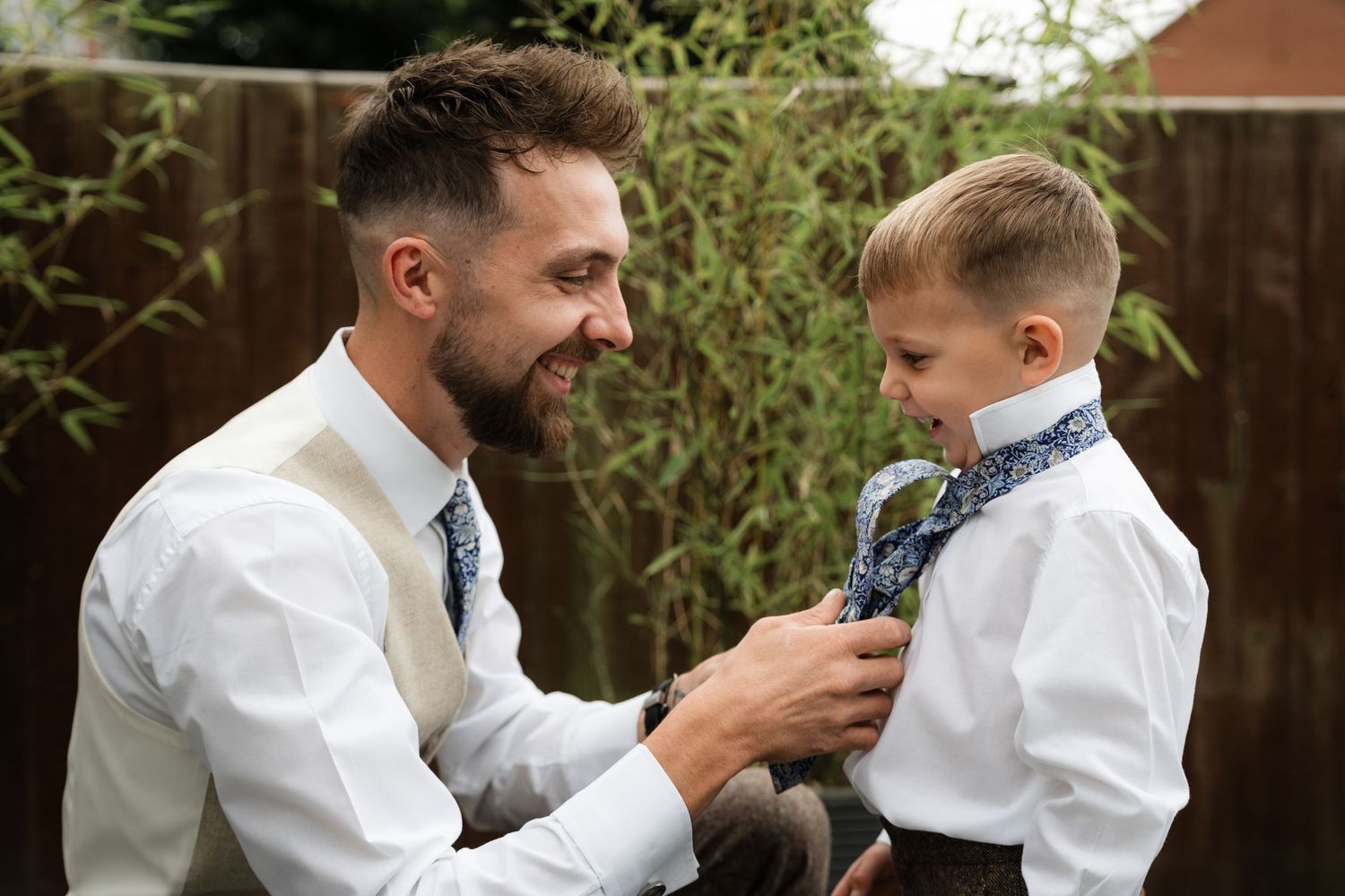 A person in a white shirt adjusts a child's tie while preparing for a formal event.
