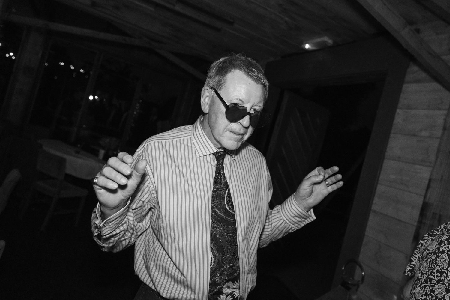 A person in a striped shirt and tie gestures while performing on stage in black and white.