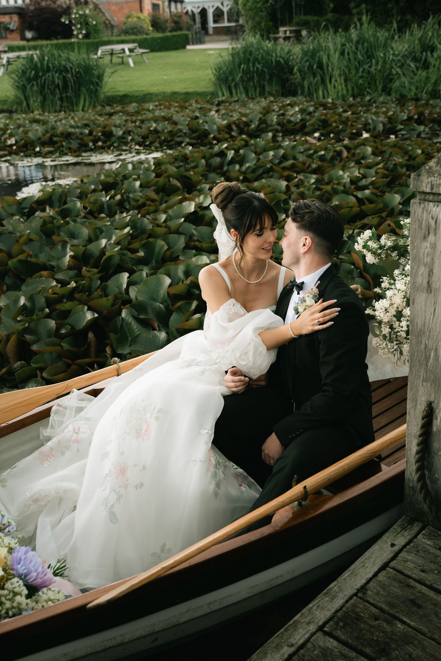 A romantic wedding couple shares intimate moments on a wooden dock overlooking a serene lily pond.